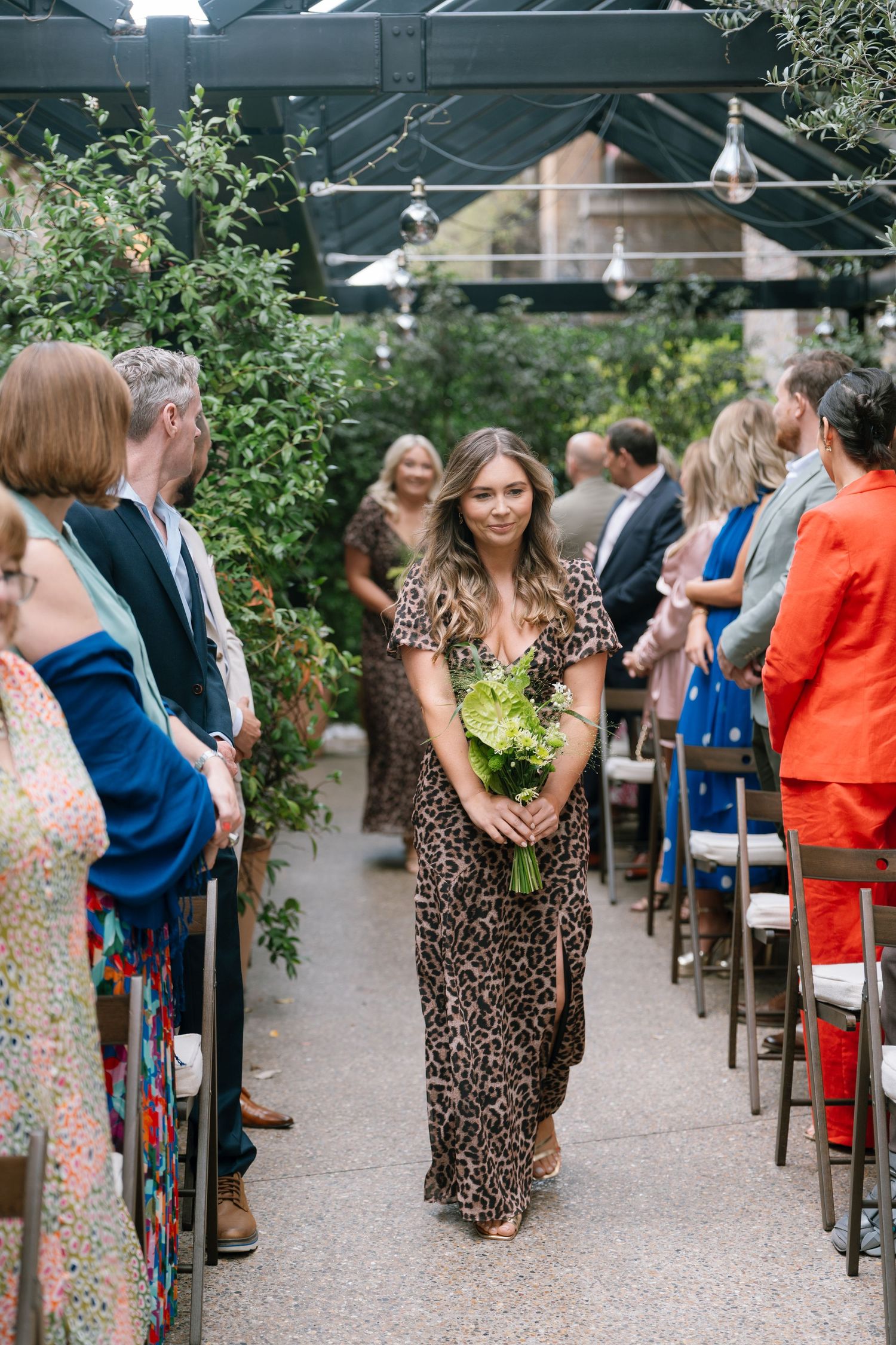 Wedding guests in colorful dresses and suits seated at an outdoor ceremony venue.