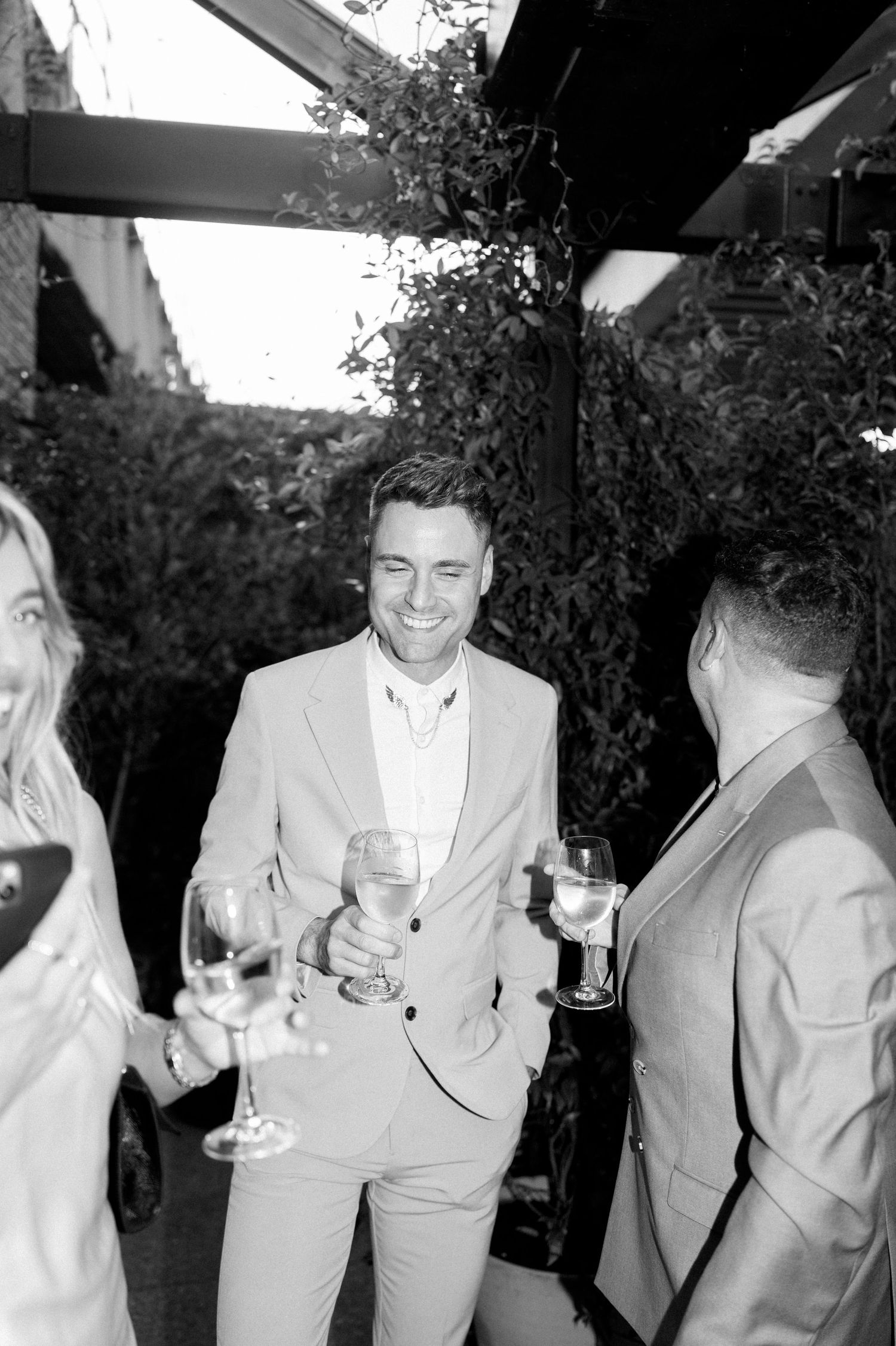 Guests enjoying drinks and conversation at an outdoor wedding reception in black and white.