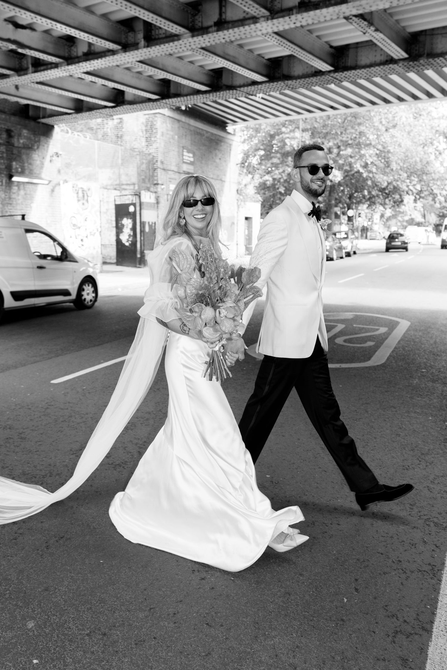 Playful wedding photos taken under an urban overpass in black and white.