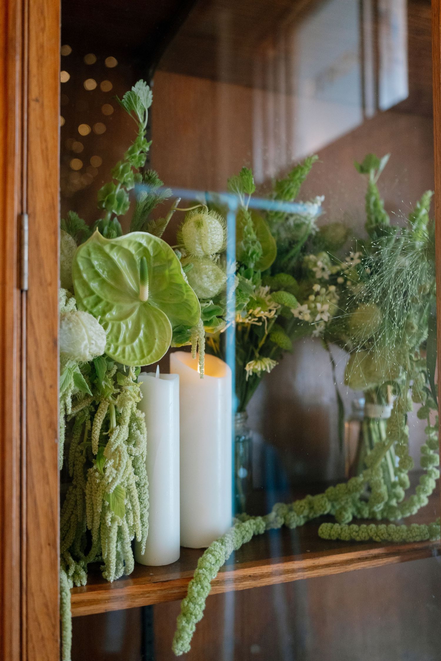 White candles and green foliage displayed in wooden window frames for elegant decor.
