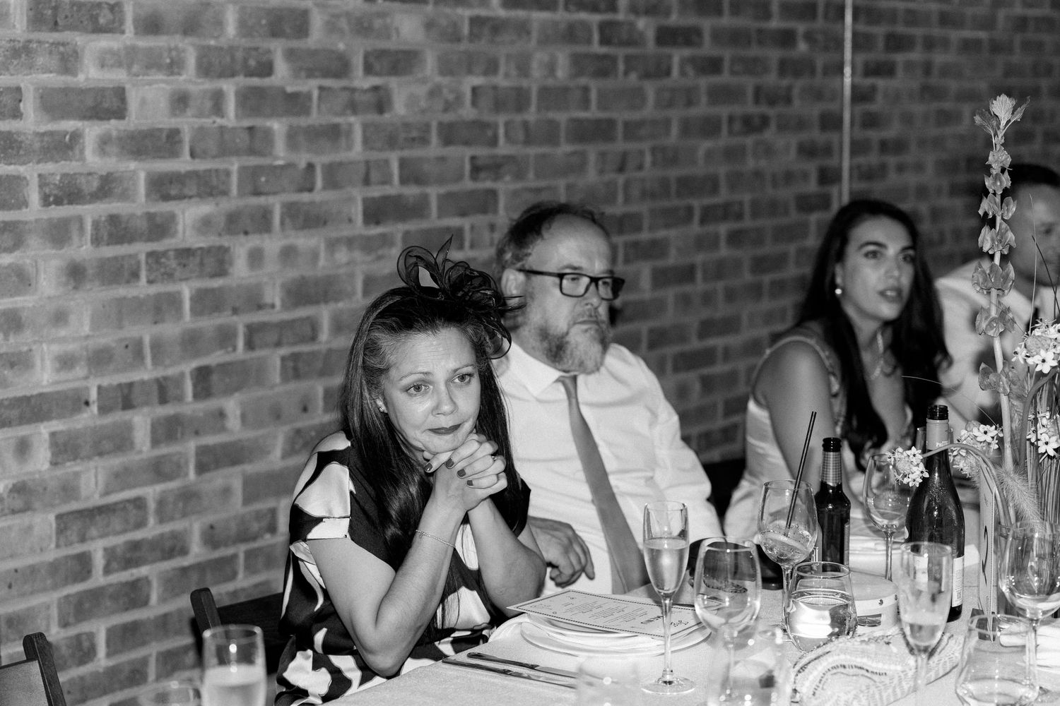 Wedding guests seated at long tables with brick wall backdrop during reception.