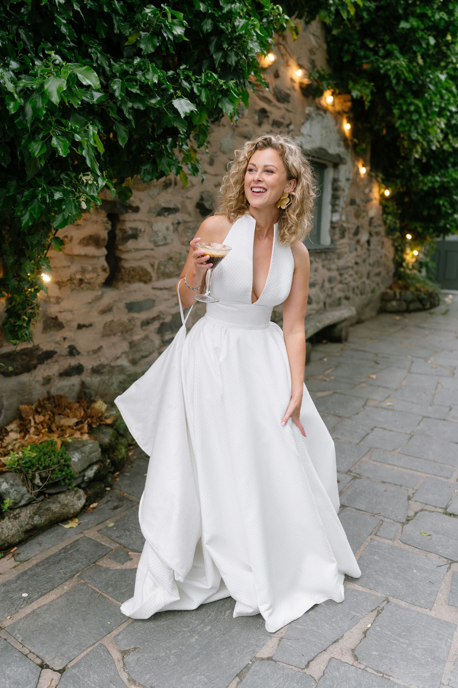 Elegant white wedding dress photographed on stone patio with green foliage and twinkle lights.
