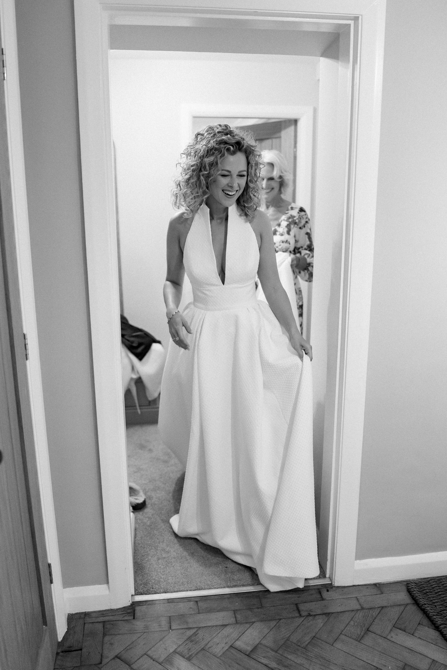 A person in an elegant white halter wedding dress stands in a doorway.
