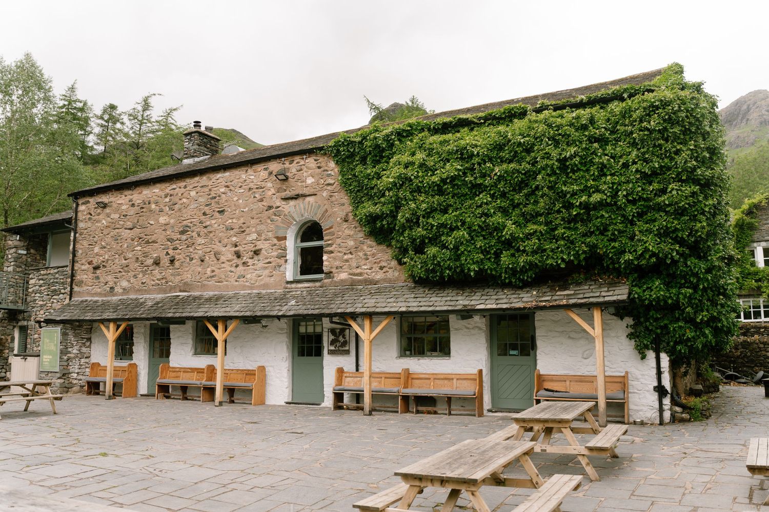 Rustic stone buildings with wooden benches and outdoor seating areas nestled in a green landscape.