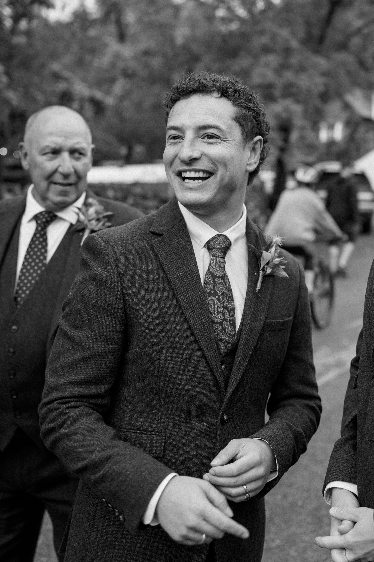Group of men in dark suits laughing together outdoors.
