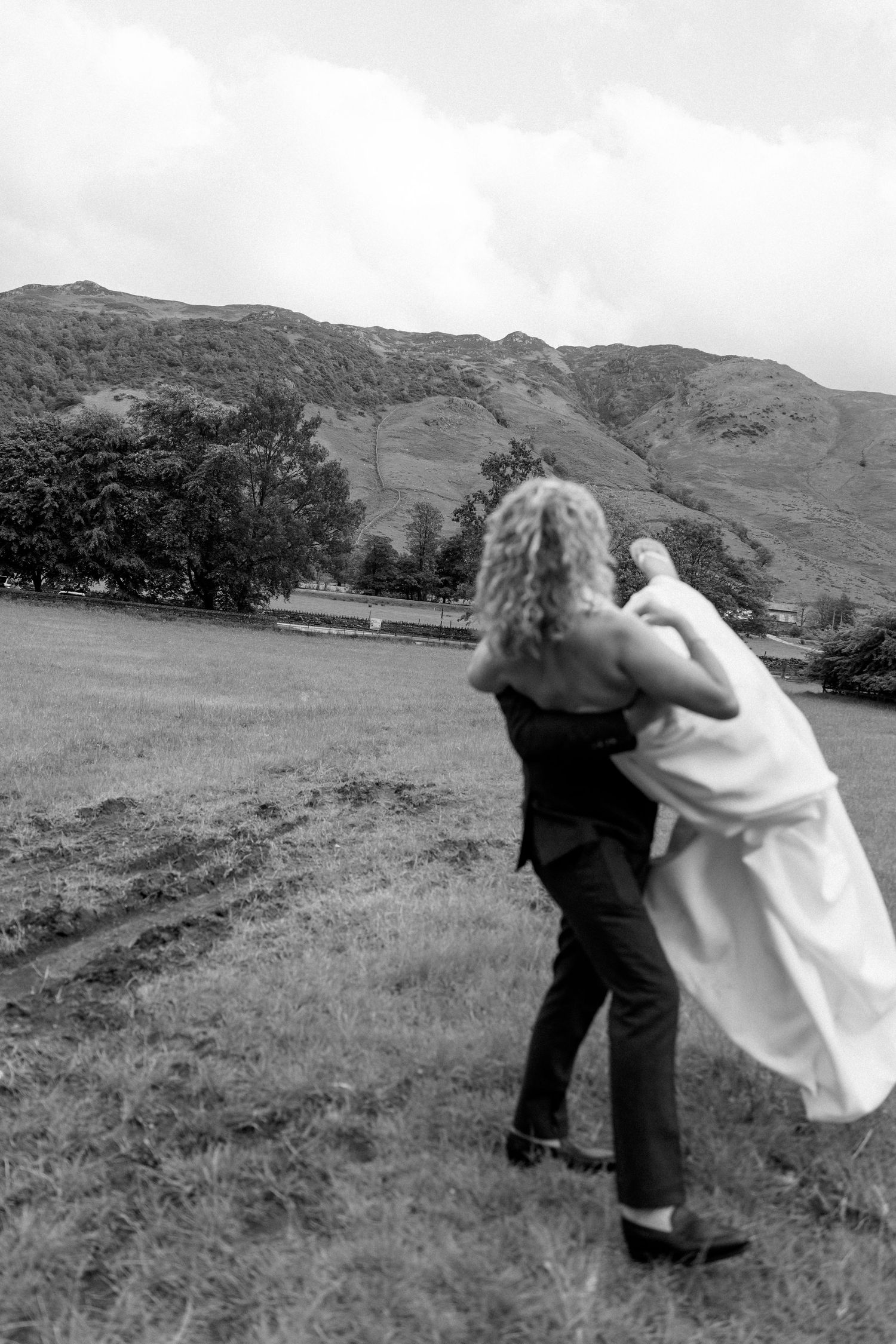 A romantic black and white moment captured against a backdrop of rolling hills.