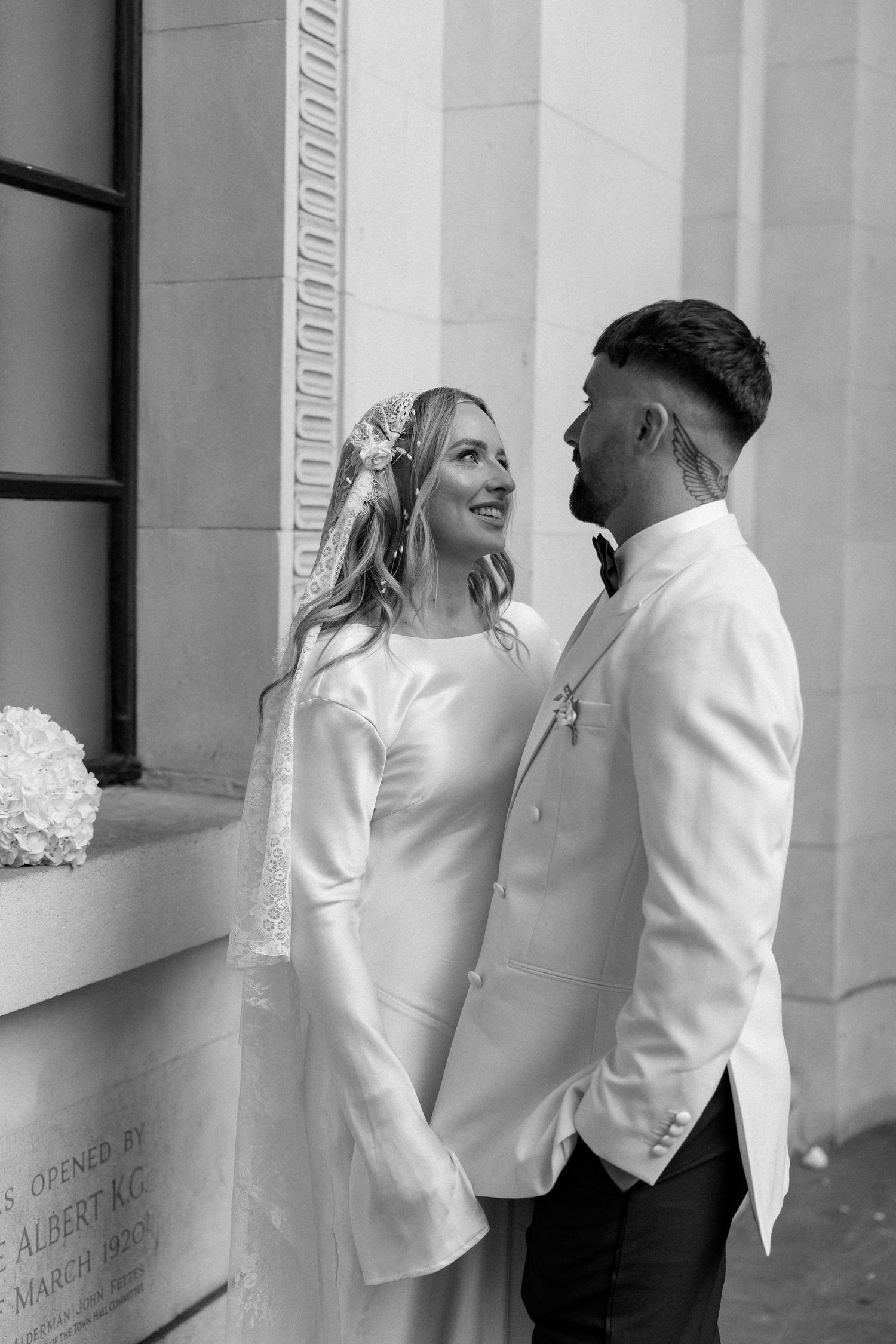 Black and white portrait of wedding couple sharing intimate moment by classical architecture.