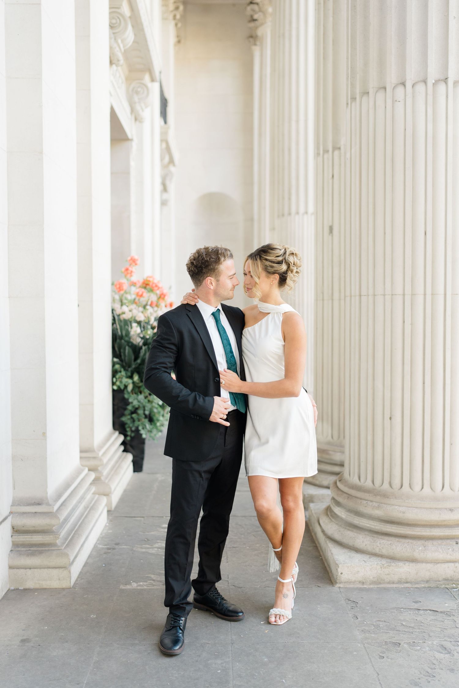 A romantic moment captured between white pillars of a grand building.
