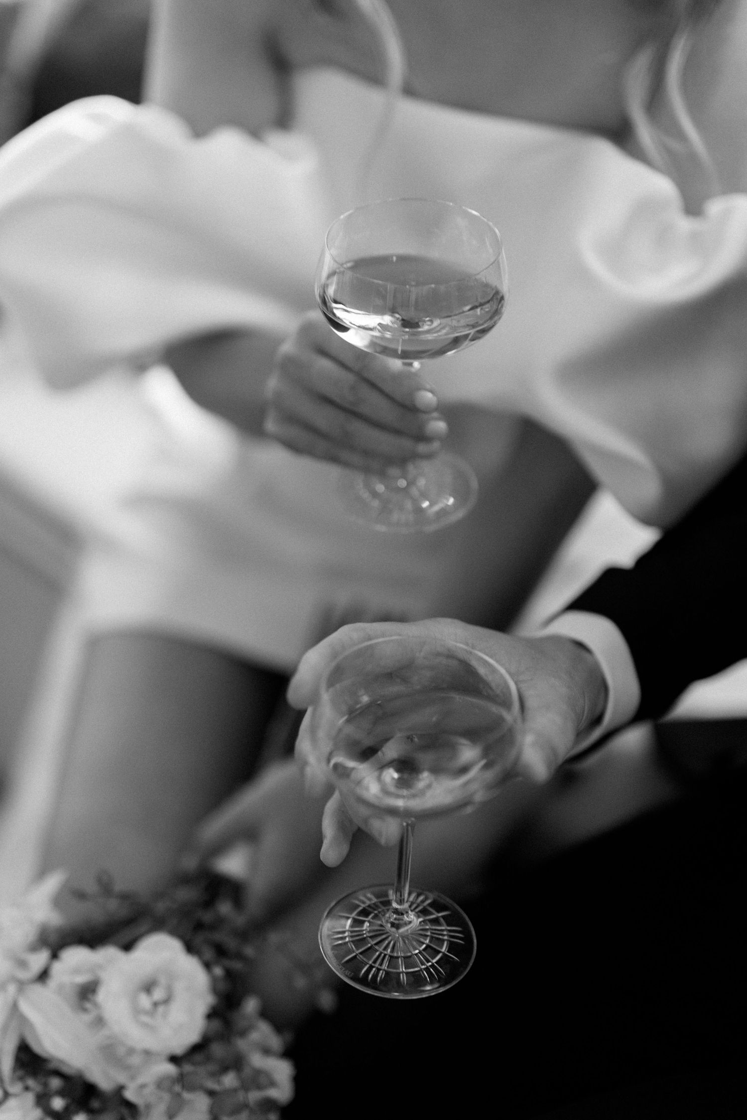 Black and white close-up of champagne glasses being held during a wedding celebration.