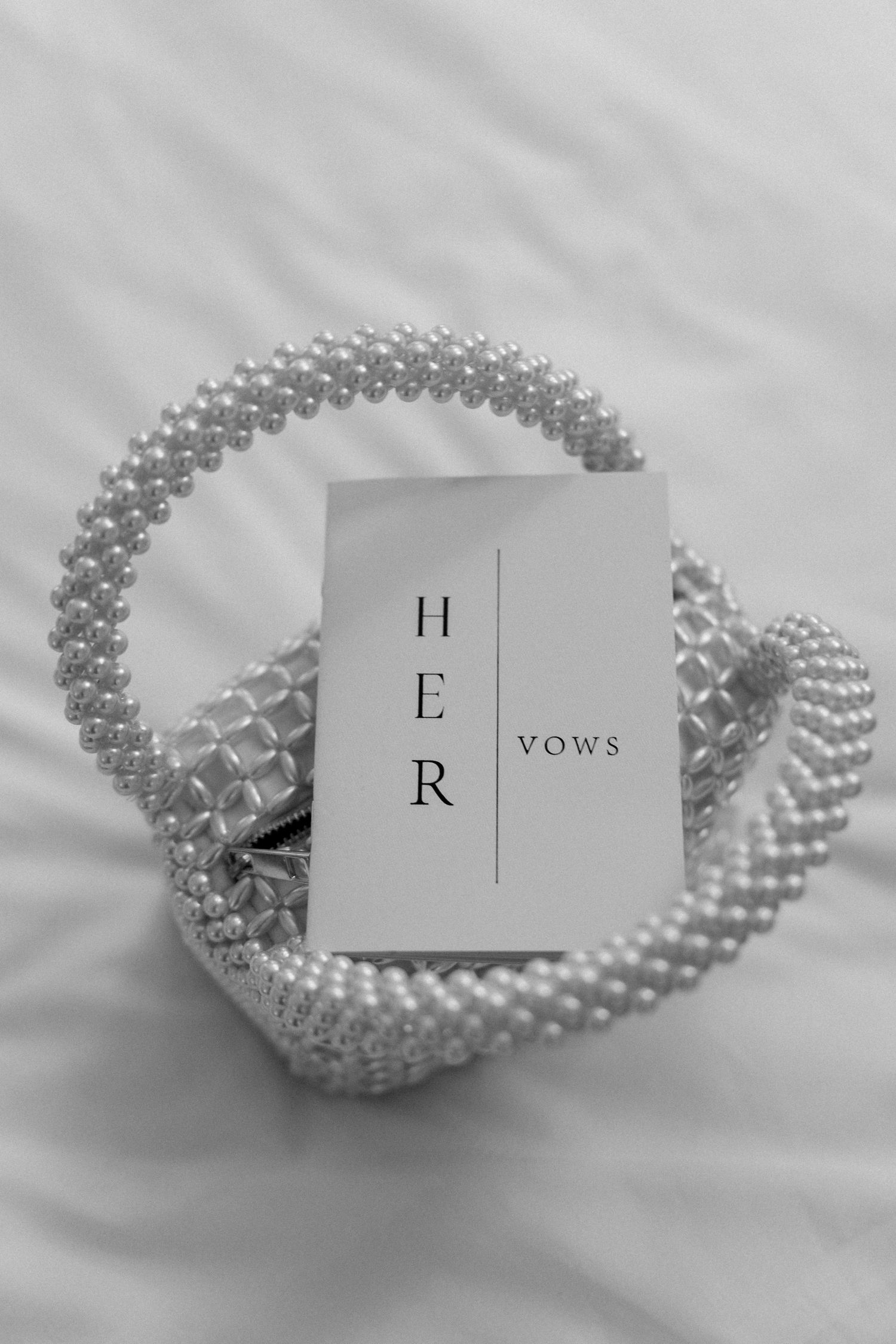 Pearl necklace with letter cards spelling out 'HER' arranged in artistic black and white composition.