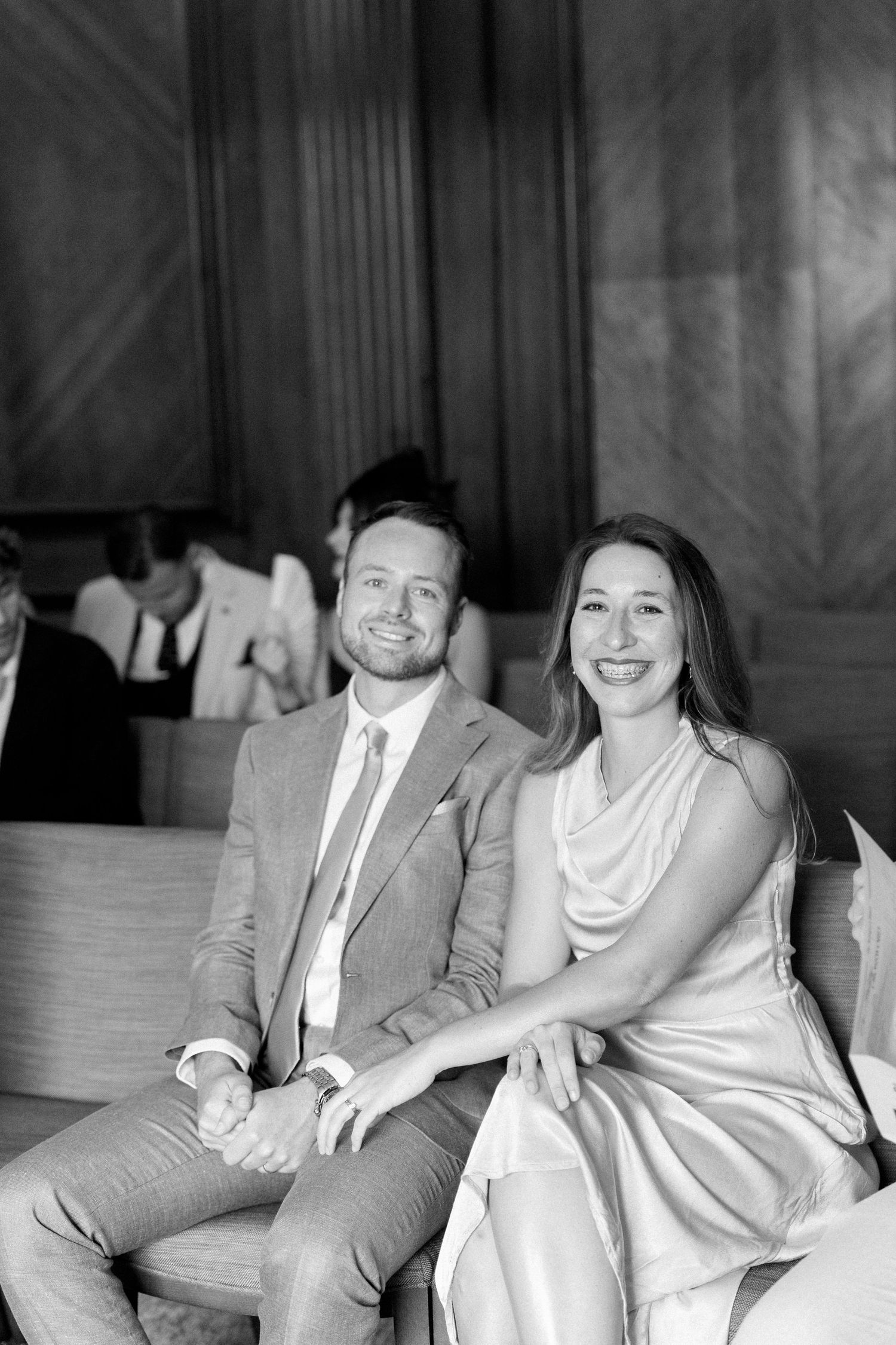 A couple sits together on a couch sharing a joyful moment in black and white photography.
