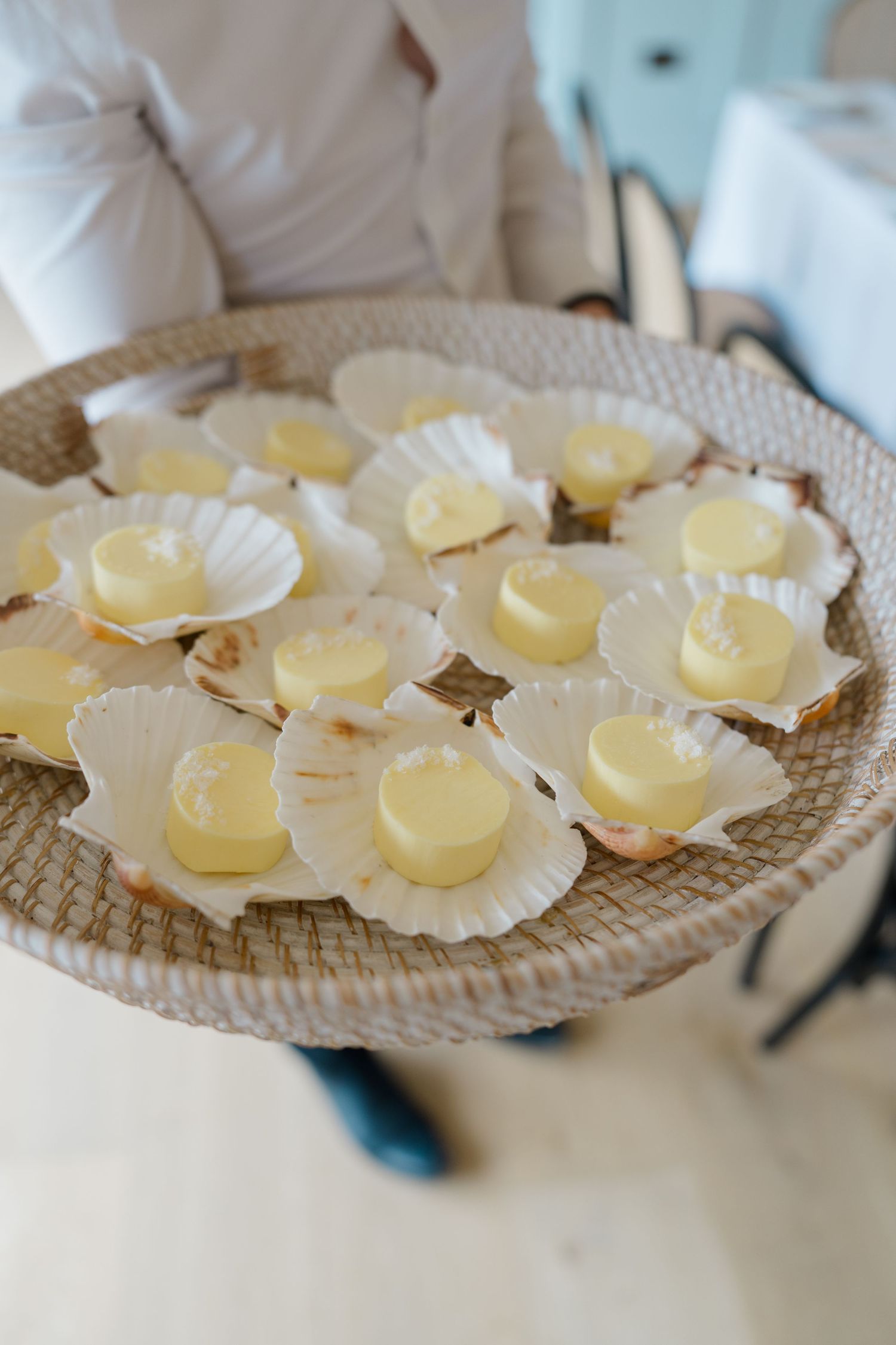 Server presents a tray of scallop shell canapes topped with creamy yellow mousse at a wedding reception.