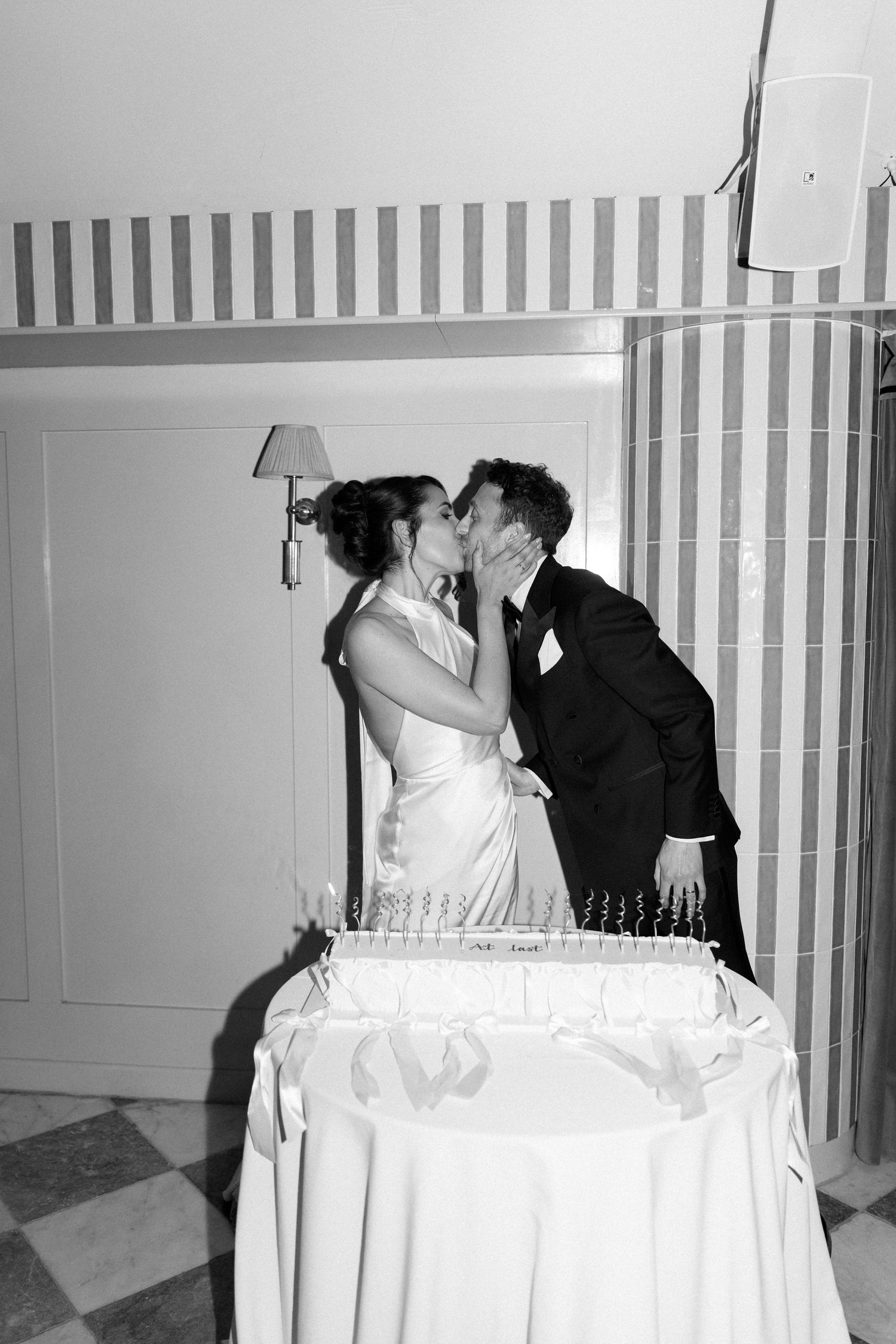 Bride and groom share a kiss behind a champagne tower in a black and white reception photo.