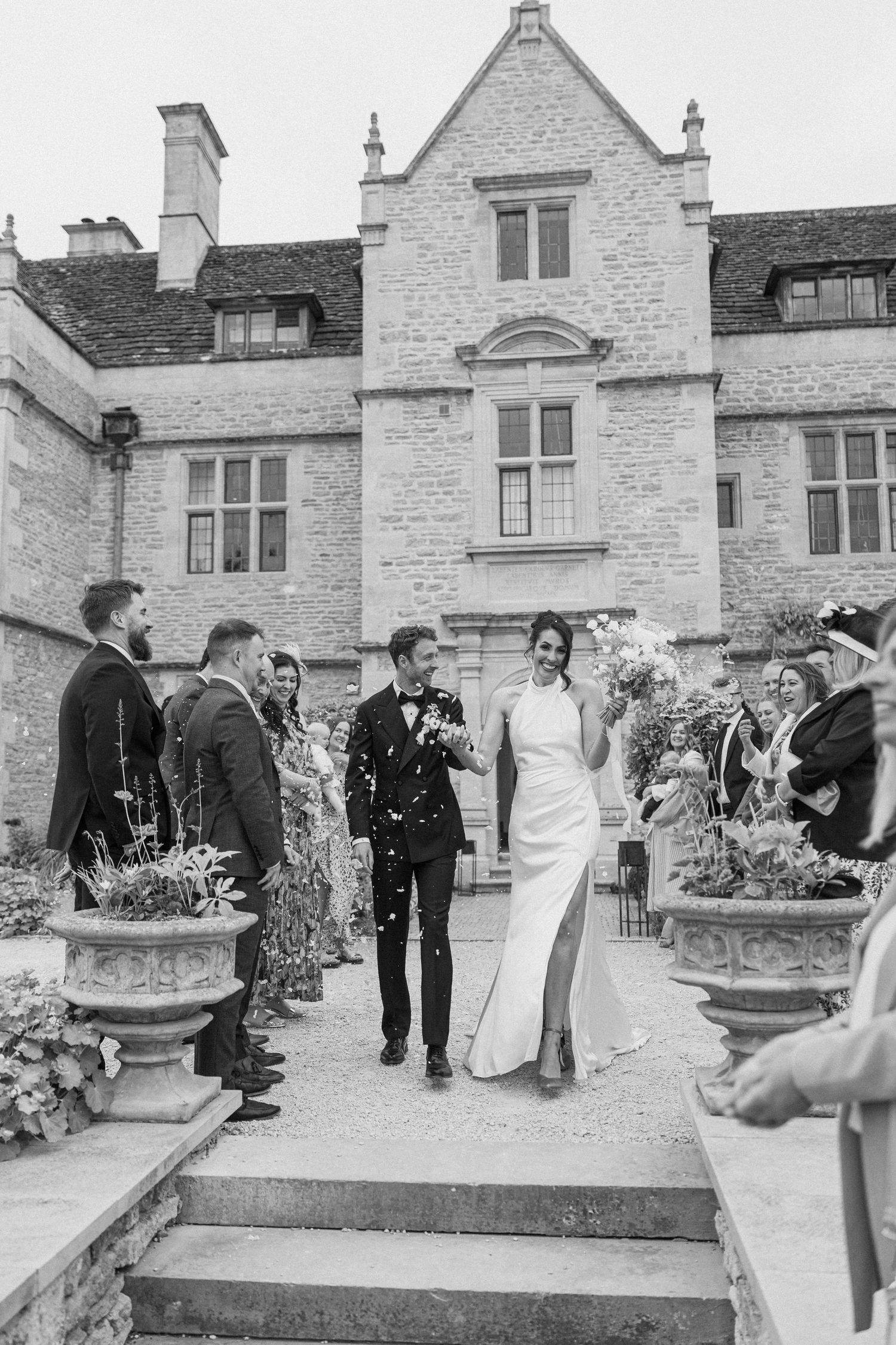 Newlyweds walk through confetti shower outside a historic stone manor after their ceremony.
