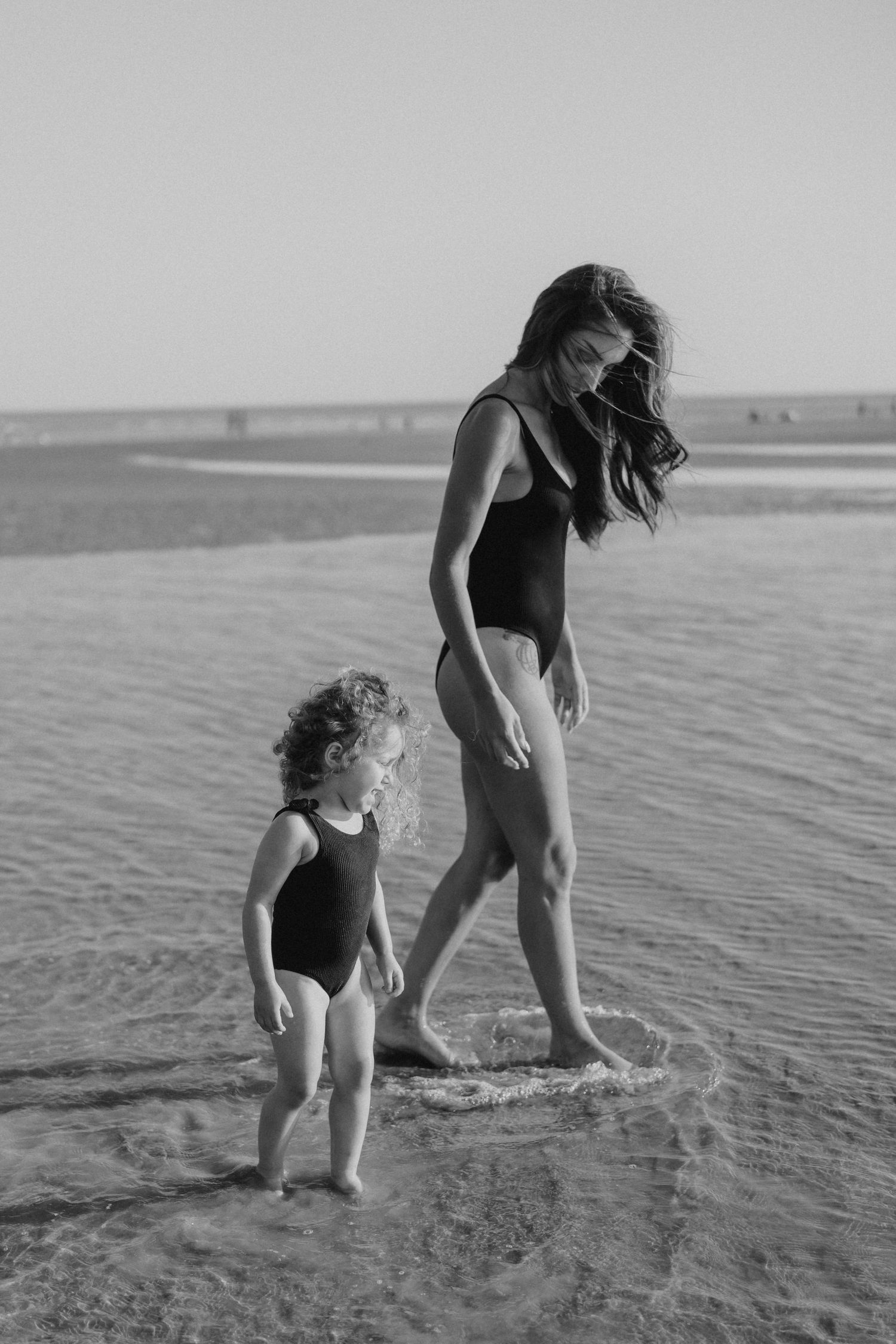 Black and white image of people walking through shallow coastal waters.
