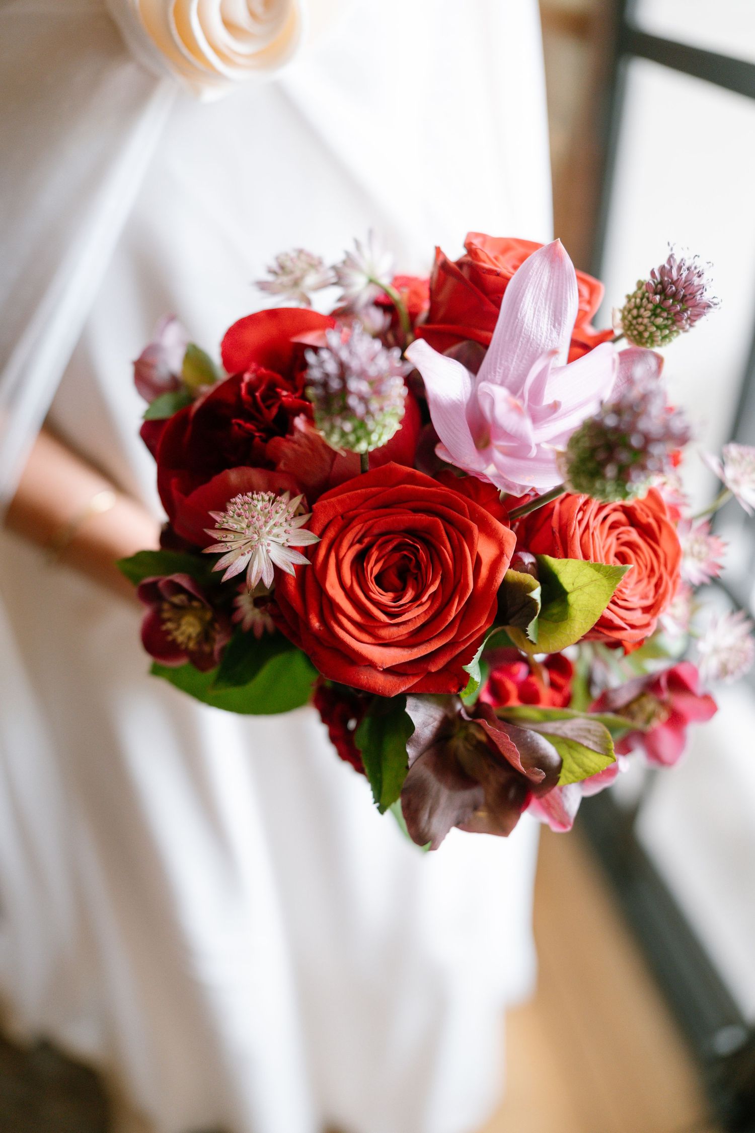Close-up of a romantic red and pink rose wedding bouquet with delicate accent flowers.