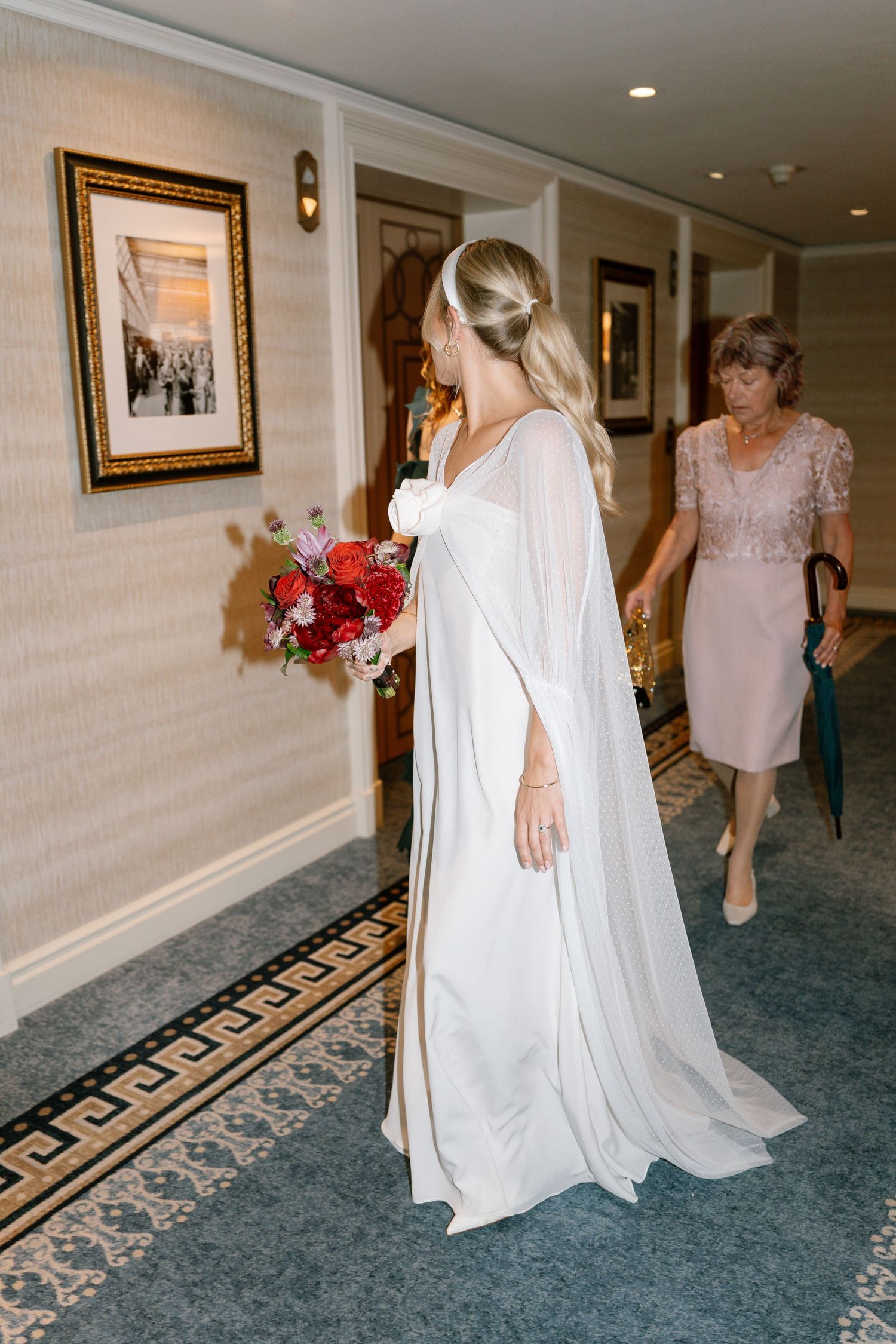 Wedding party walking down ornate hotel corridor with patterned carpet.
