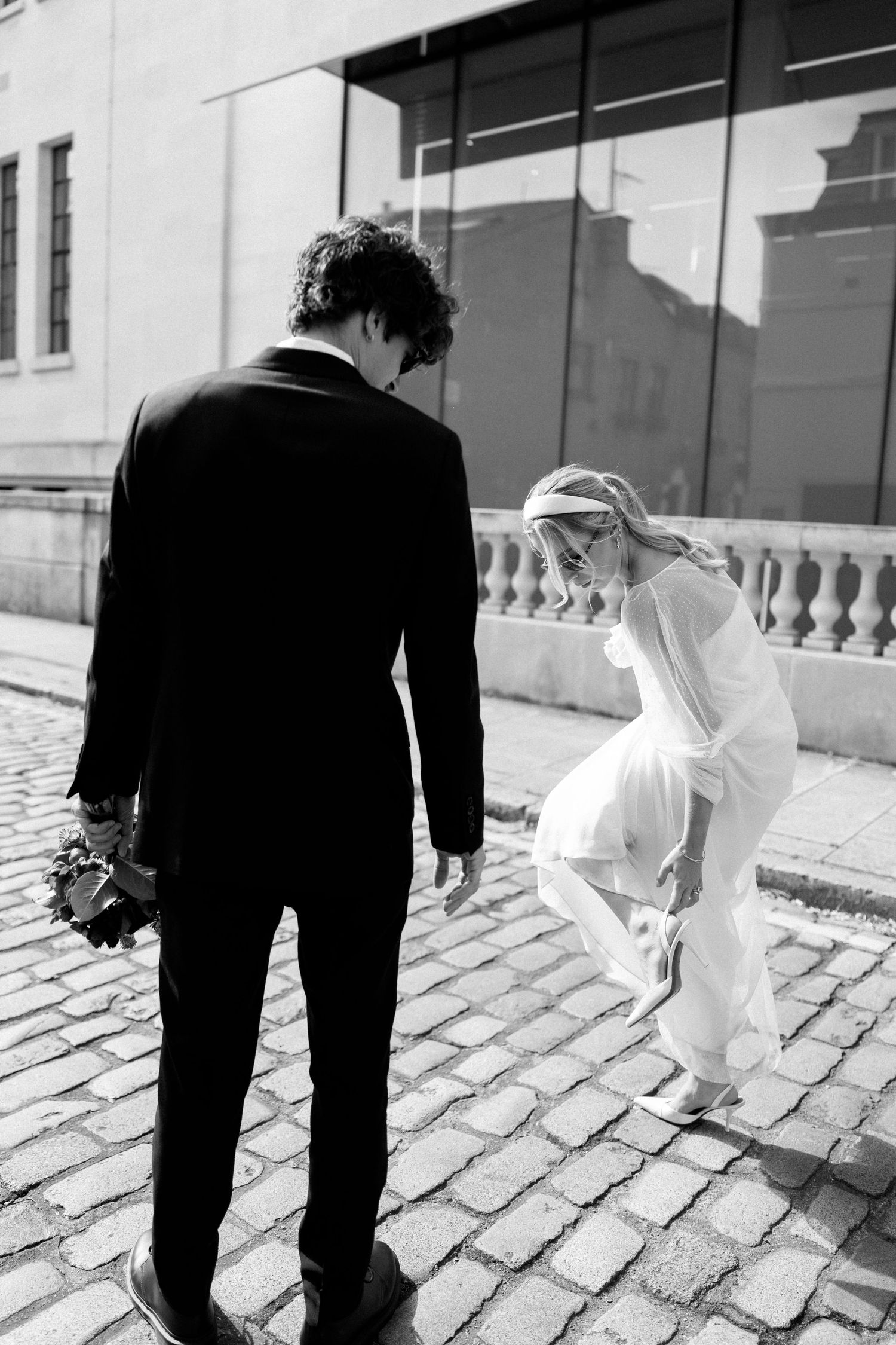 Black and white photo of a couple walking on cobblestone streets with flowing dress movement.