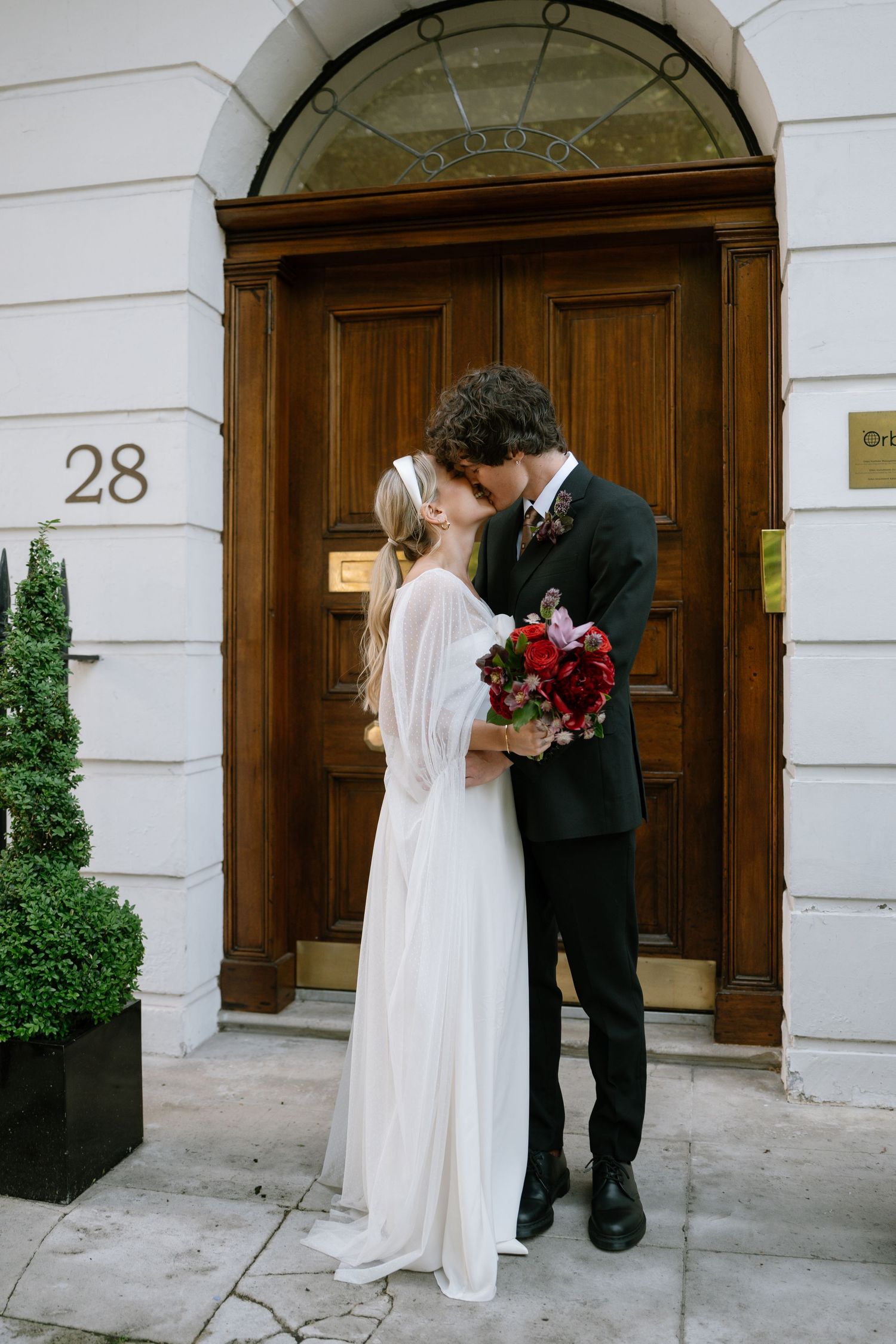 A couple shares a romantic moment in front of an elegant doorway numbered 28.