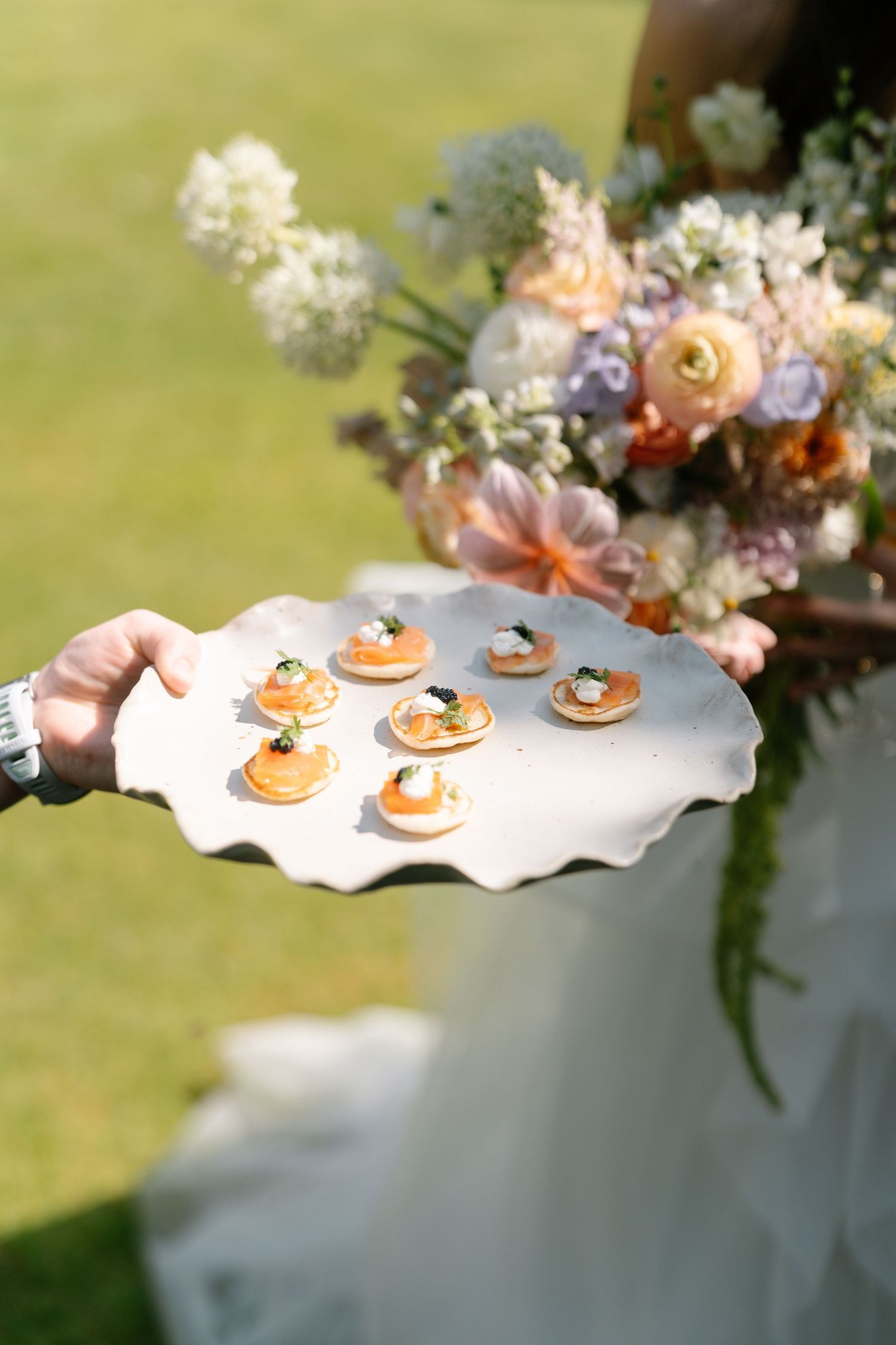 Elegant pastries displayed on a white scalloped serving platter with floral arrangements in the background.