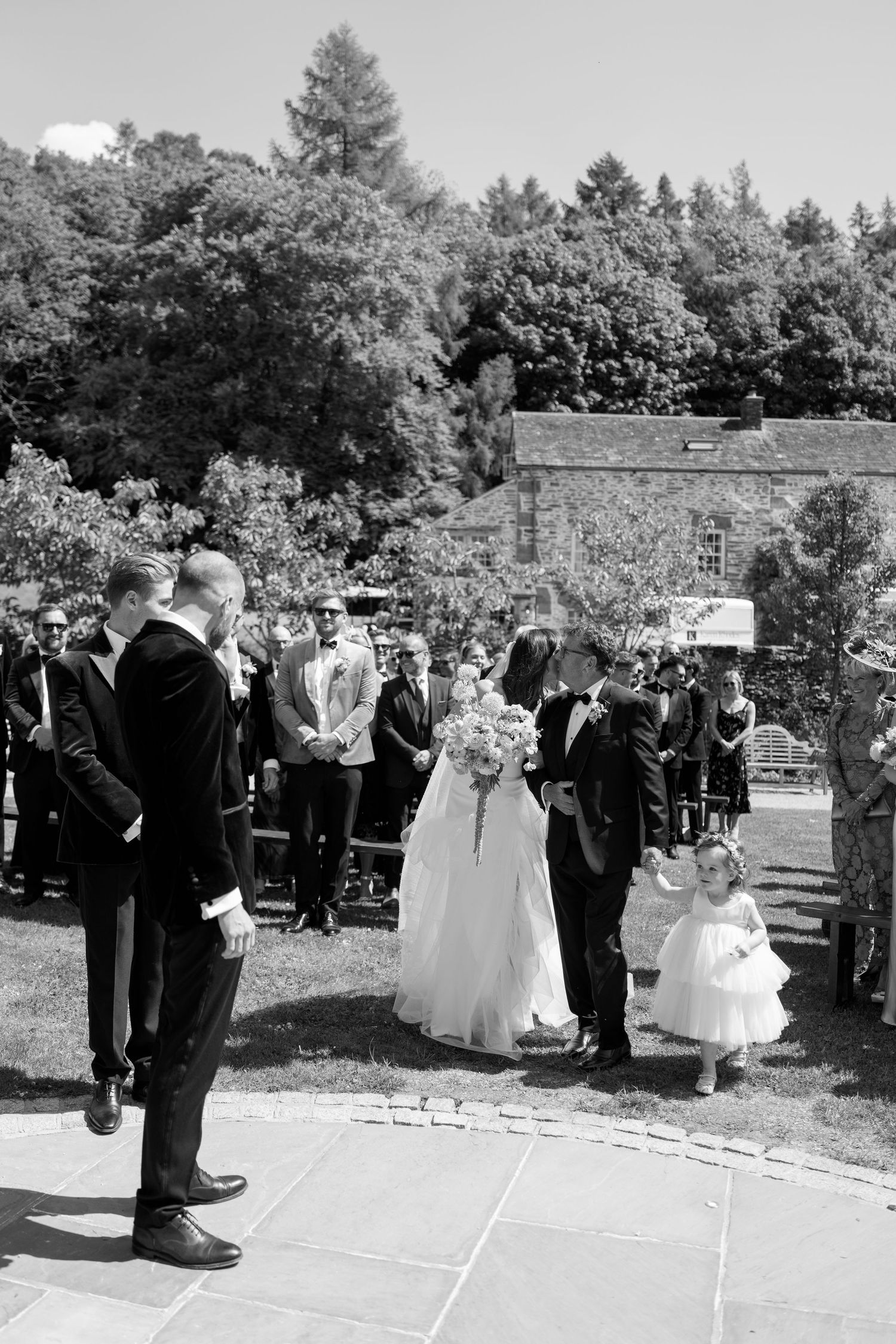 Black and white photo of wedding ceremony lineup on stone pathway.