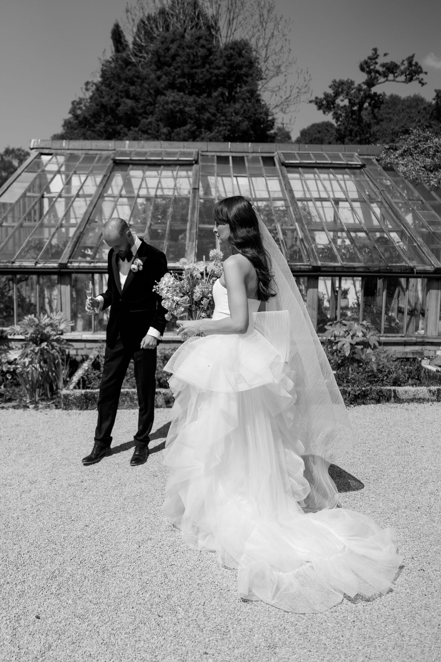 A black and white wedding photo showing a couple by vintage greenhouses.