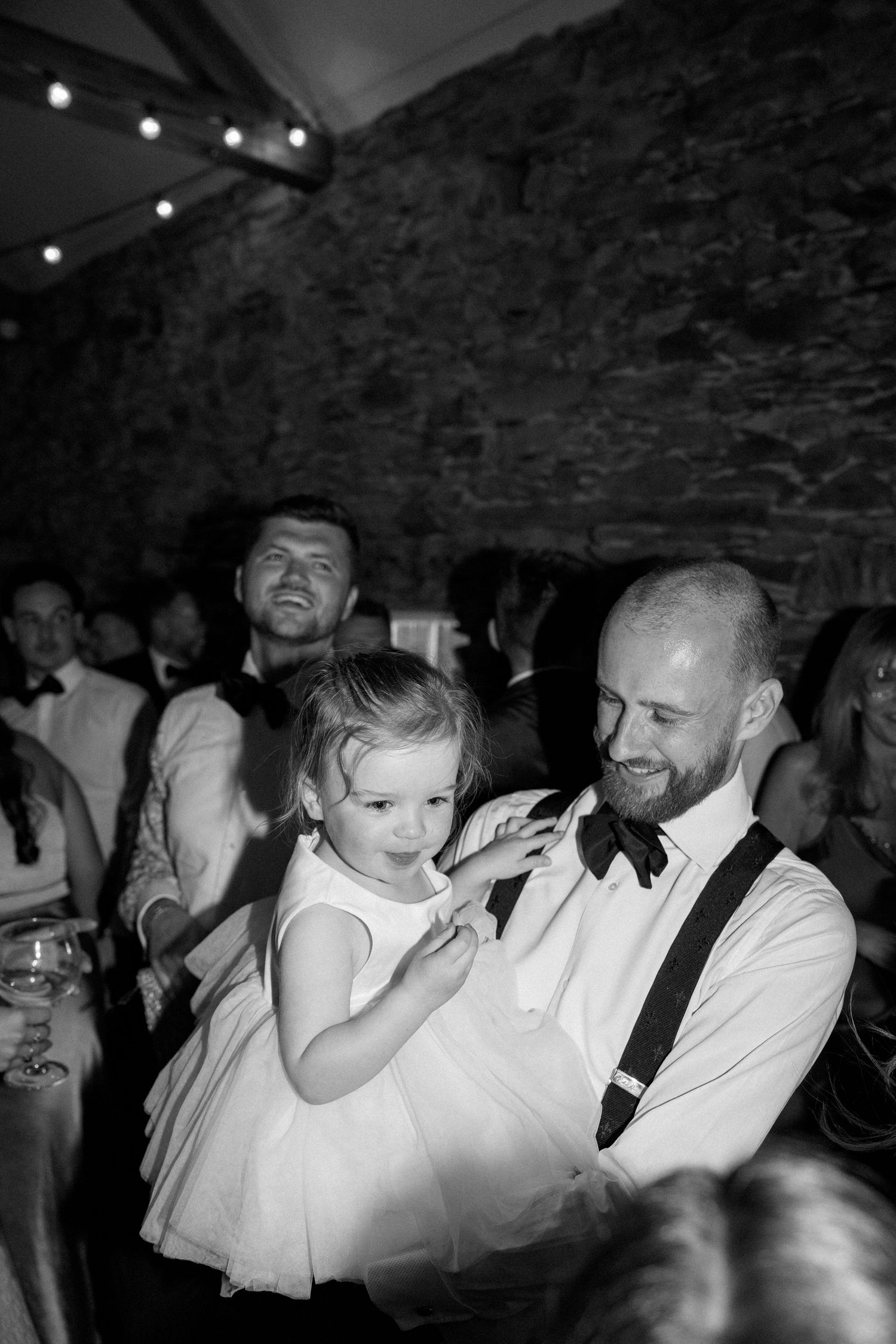 A young flower girl in white dress dances with guests during wedding reception.