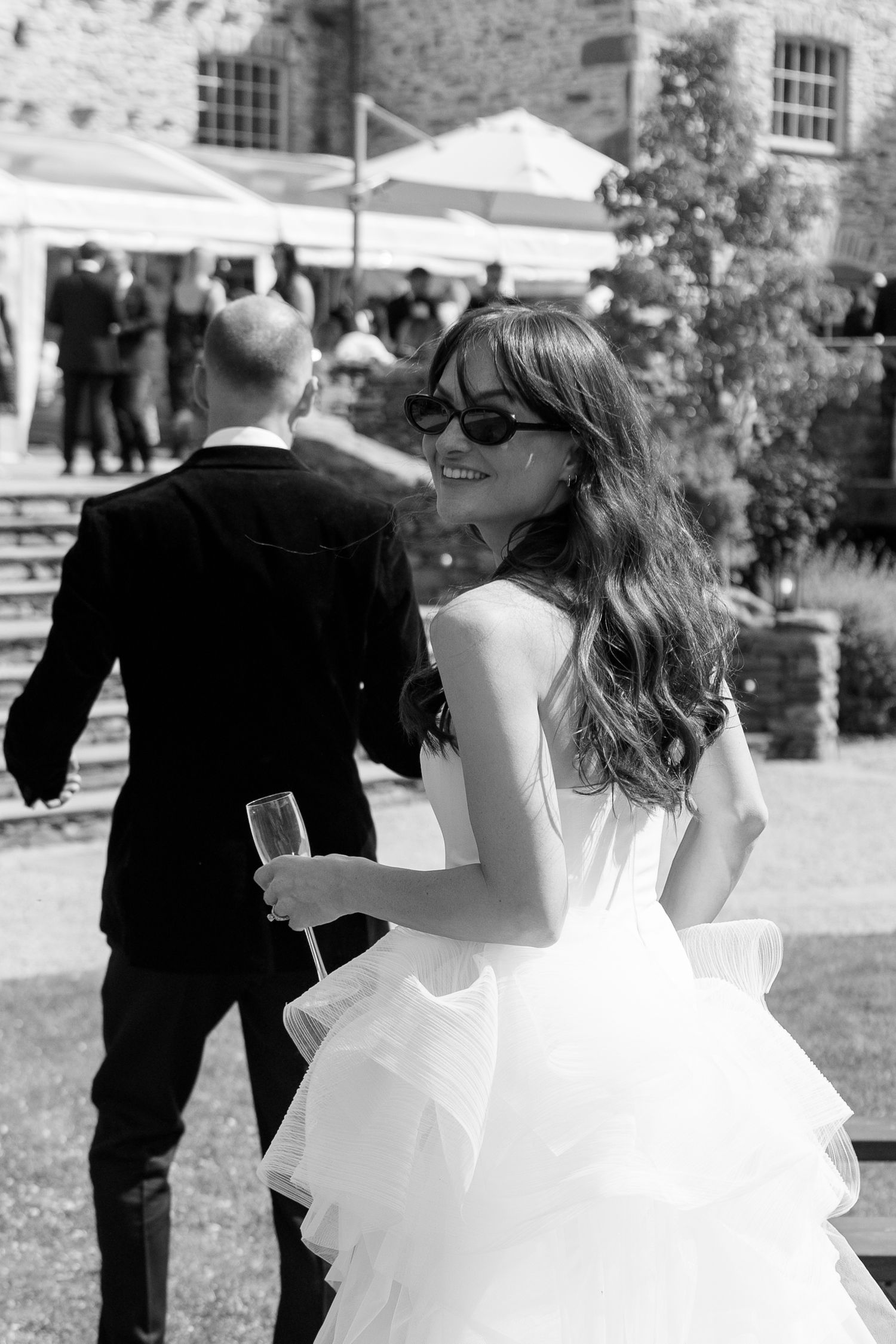 A couple in wedding attire dances together at an outdoor venue with stone buildings in the background.