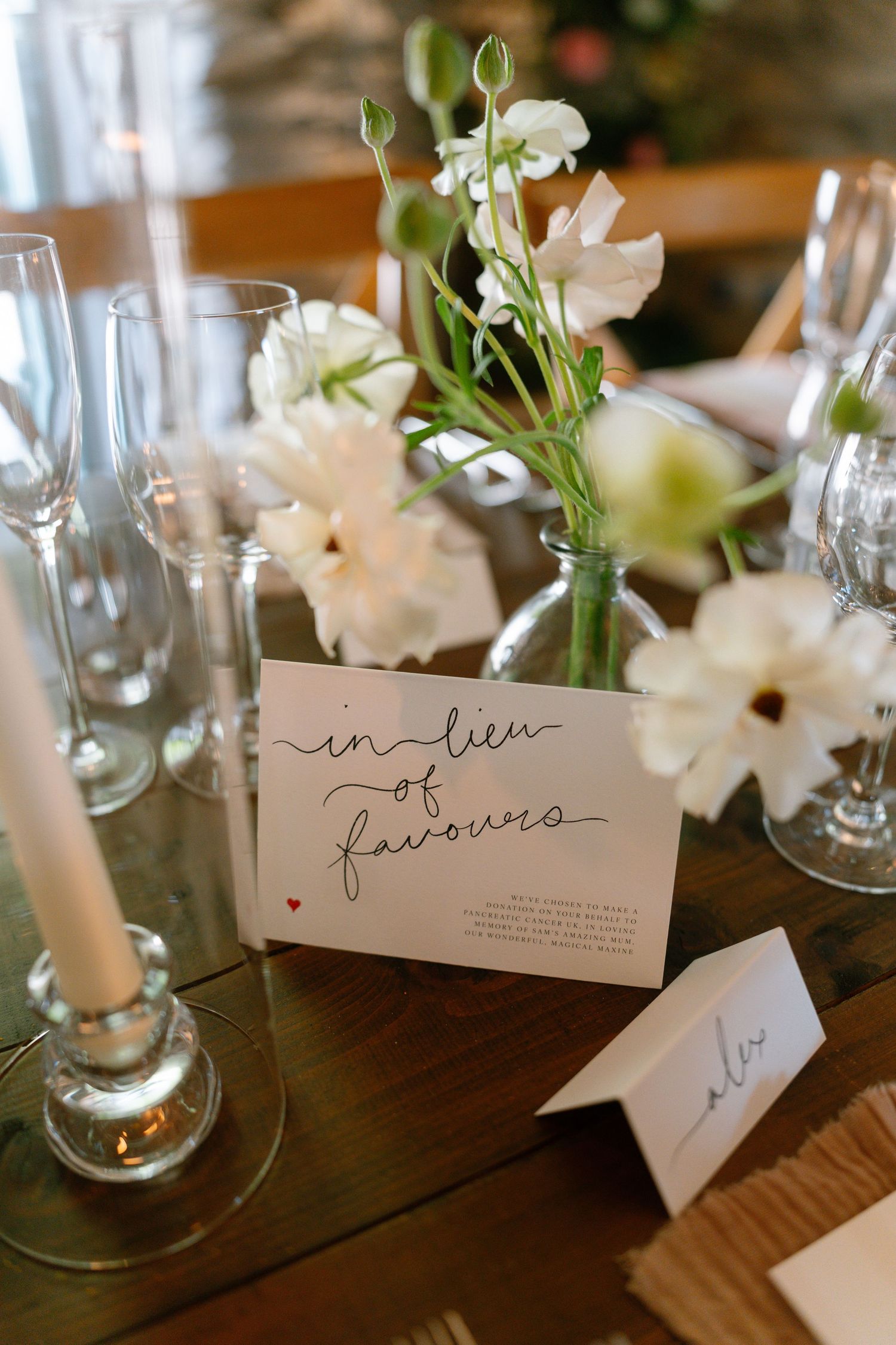 Delicate handwritten name cards displayed alongside white flowers in glass vases at a formal table setting.