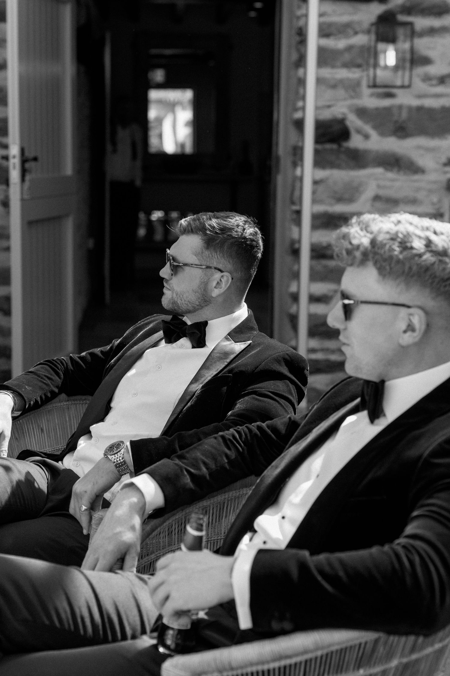 Groomsmen in formal attire relaxing in chairs during wedding festivities.
