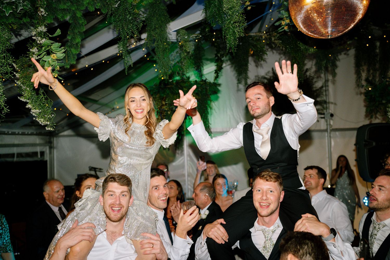 Wedding celebration with guests dancing under green lighting and disco ball.