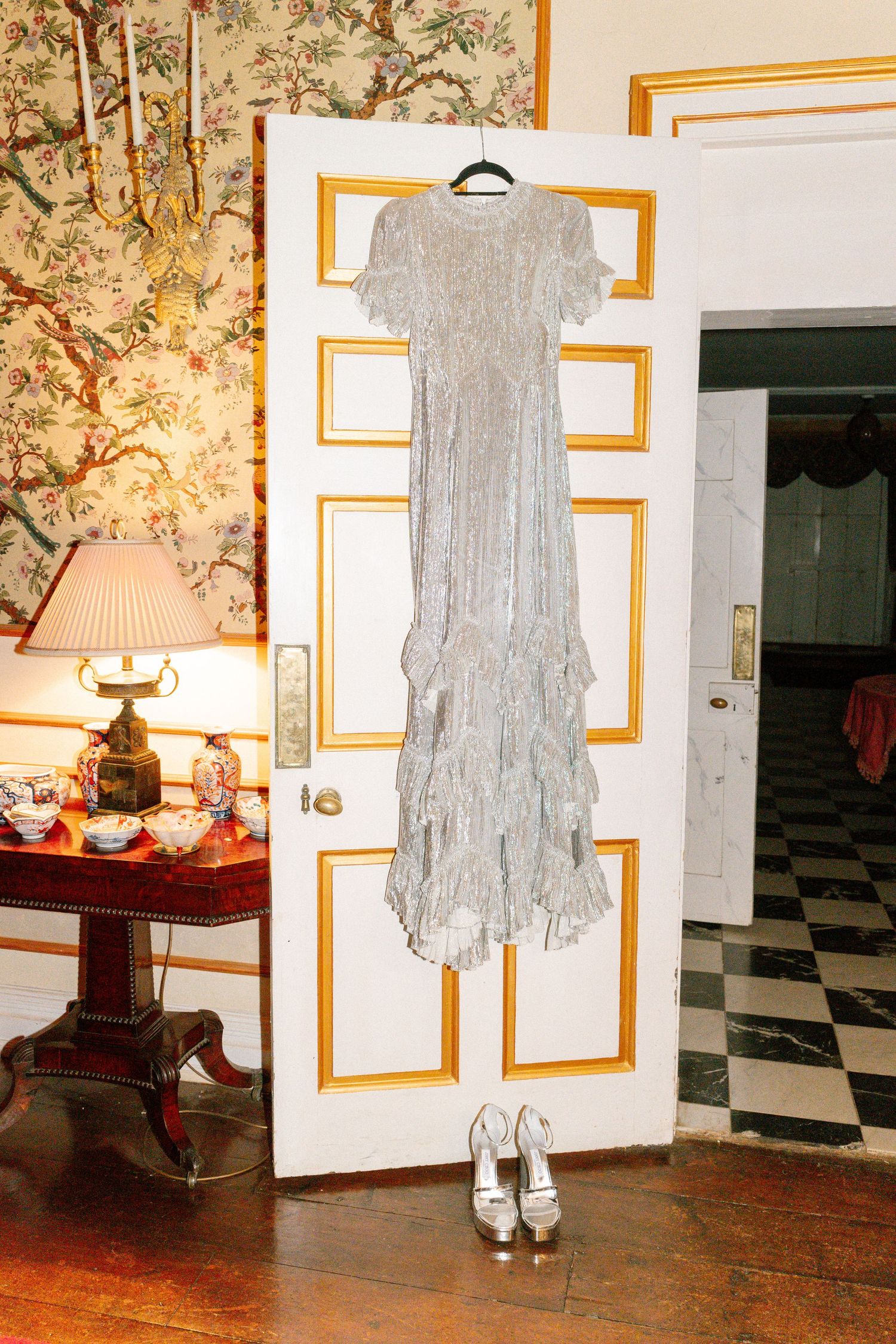 Silver sequined dress hanging on white door with gold trim and vintage decor.