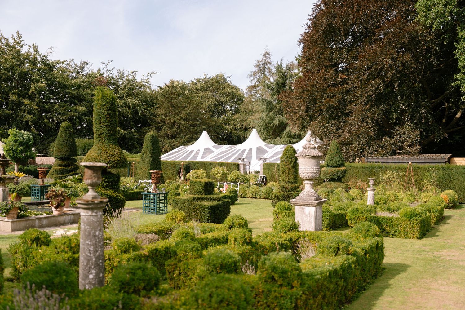 Elegant garden path lined with ornate stone pillars and manicured hedges in a formal estate setting.