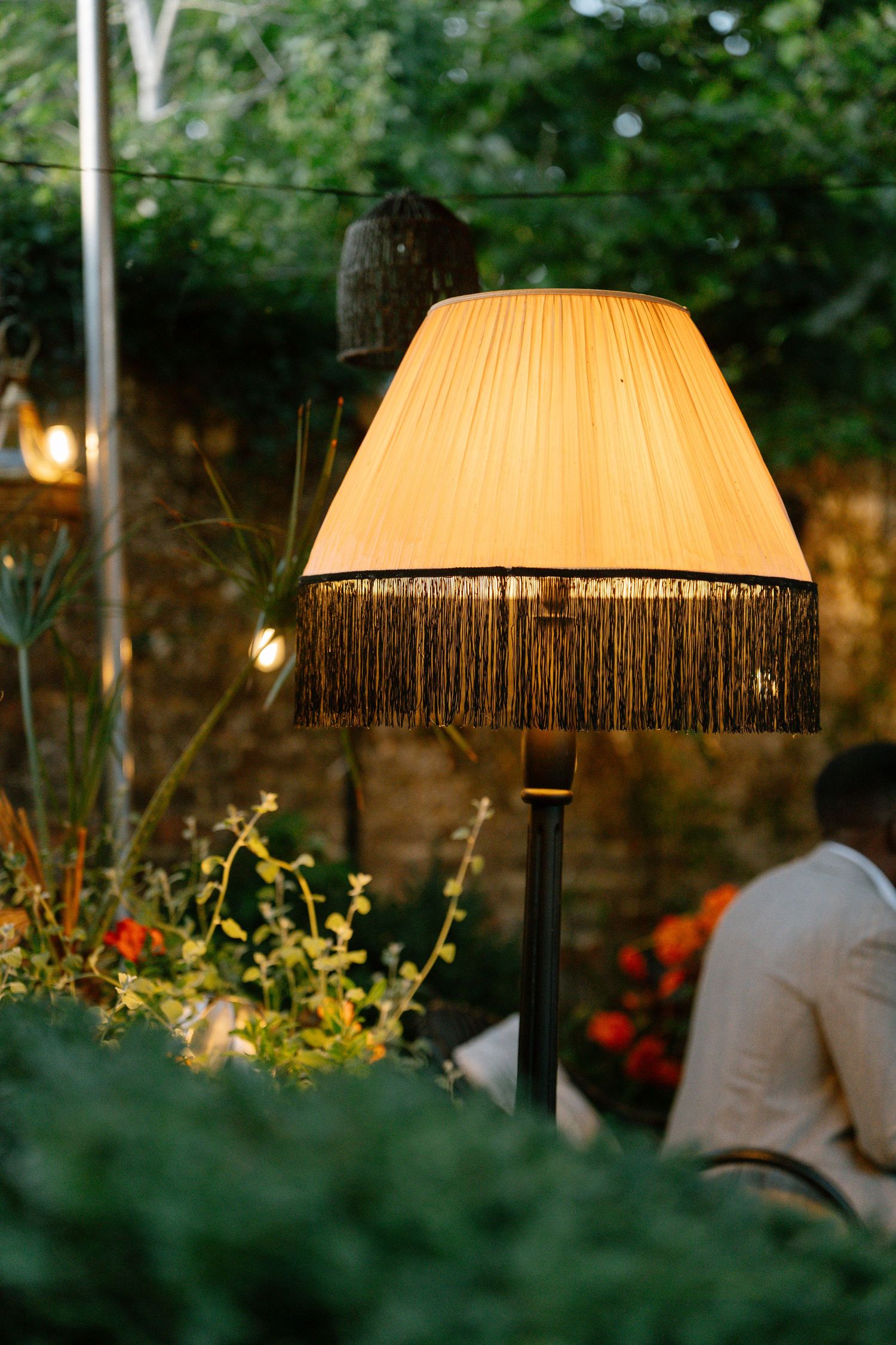 Vintage fringed lampshade glowing warmly in an outdoor garden setting at dusk.