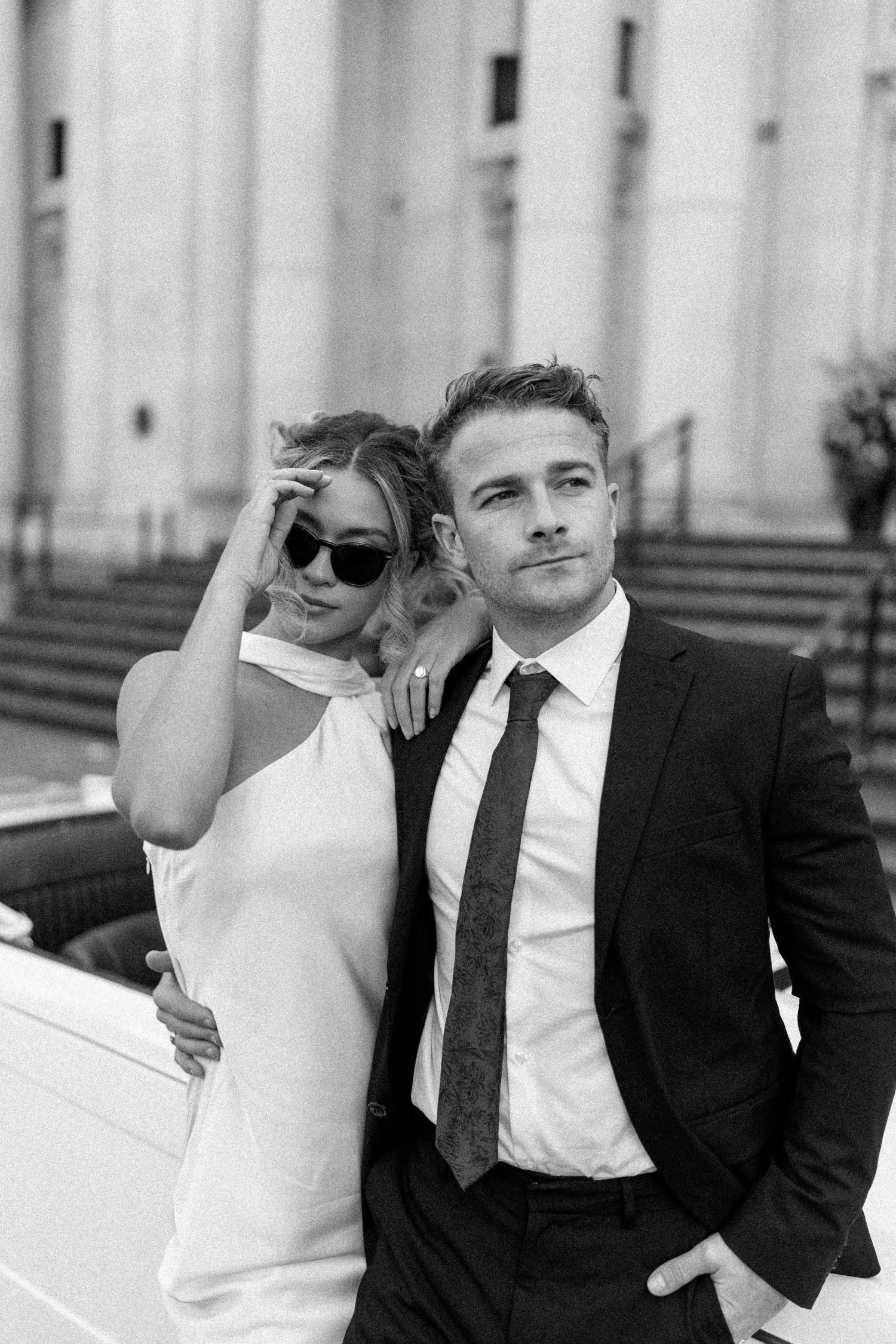 Black and white portrait of couple in formal attire posing against columned building.