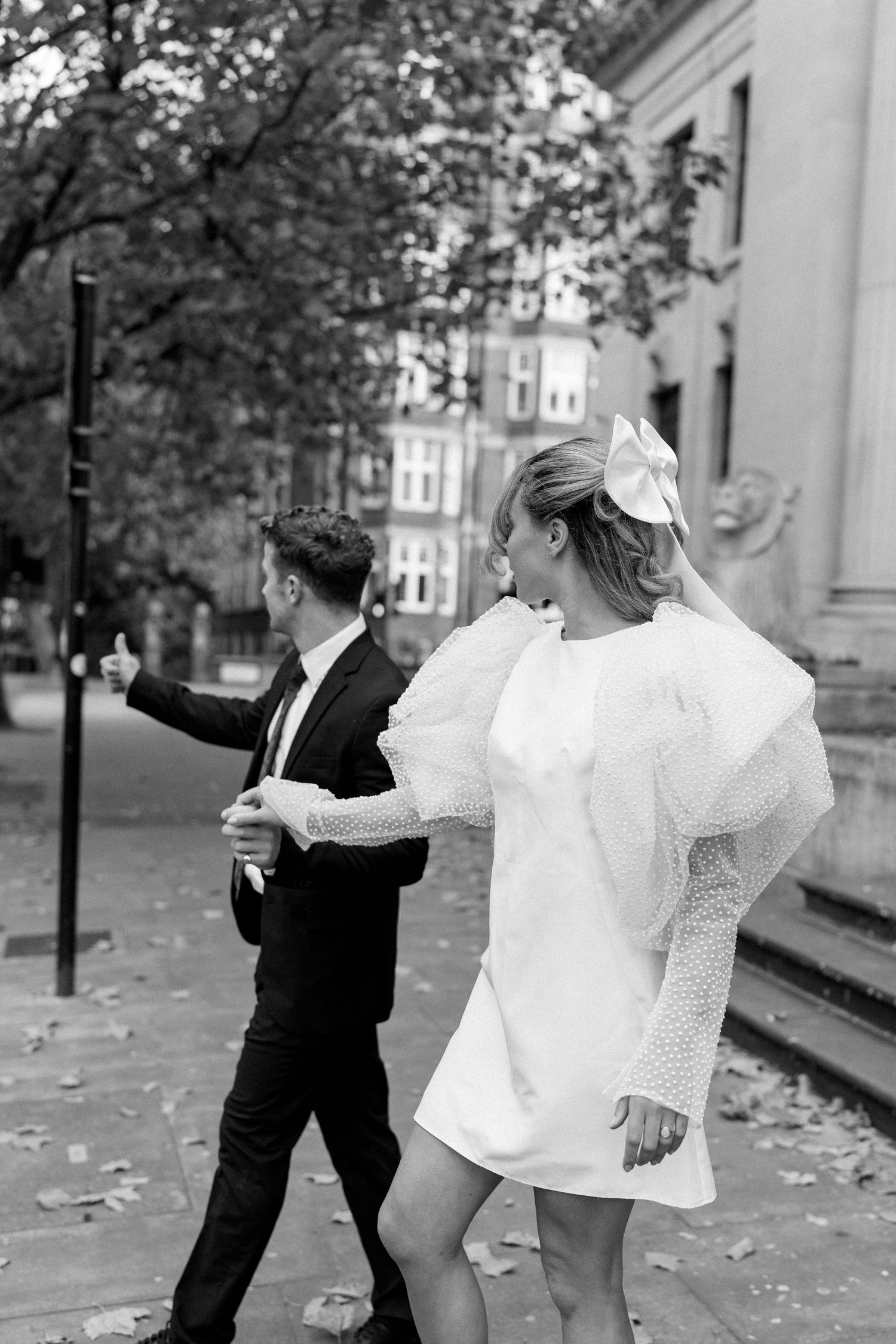 Black and white photo of a couple dancing playfully among autumn leaves.