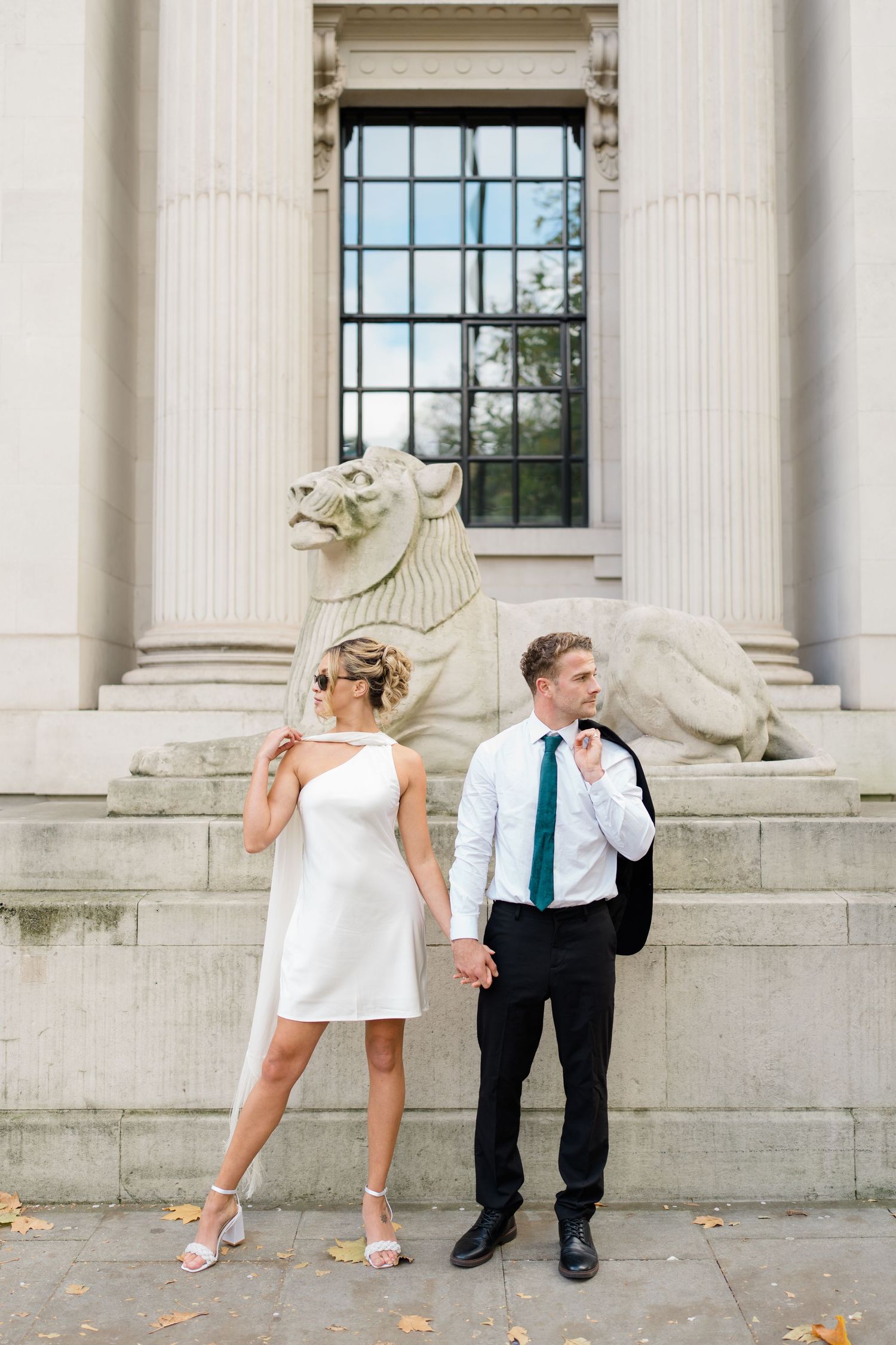 Playful couple poses on stone steps between classical white columns.