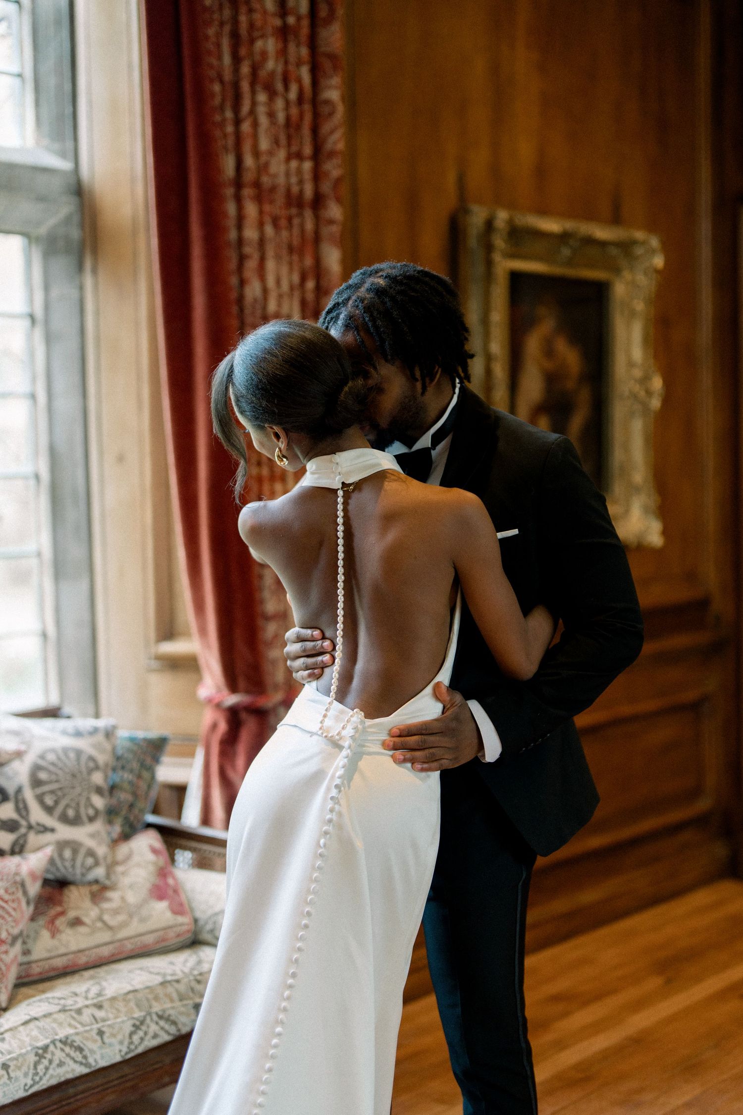 Wedding dress being prepared and buttoned up in an elegant room with wood paneling.