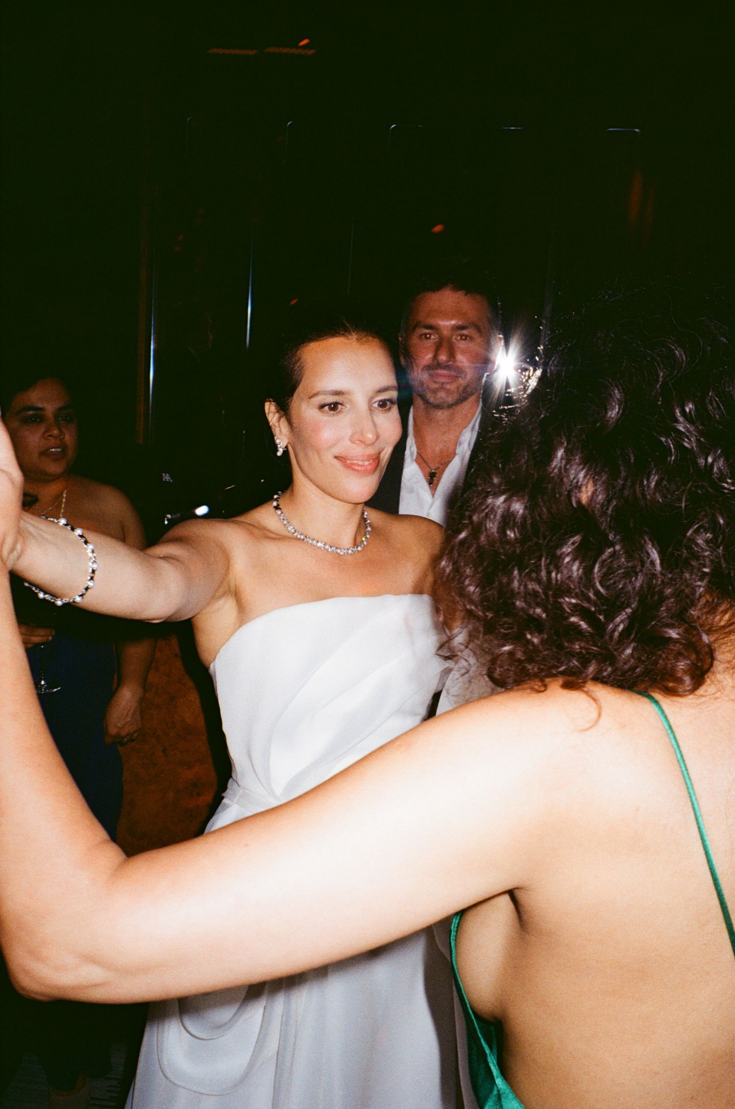 People dancing and celebrating at a wedding reception in formal attire with dim lighting.