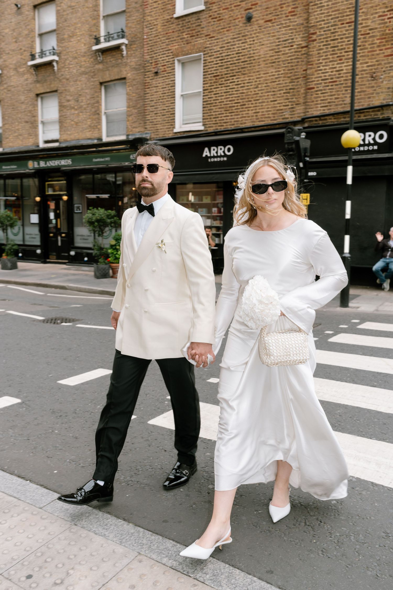 A couple in coordinated white and black attire walks across a city crosswalk.