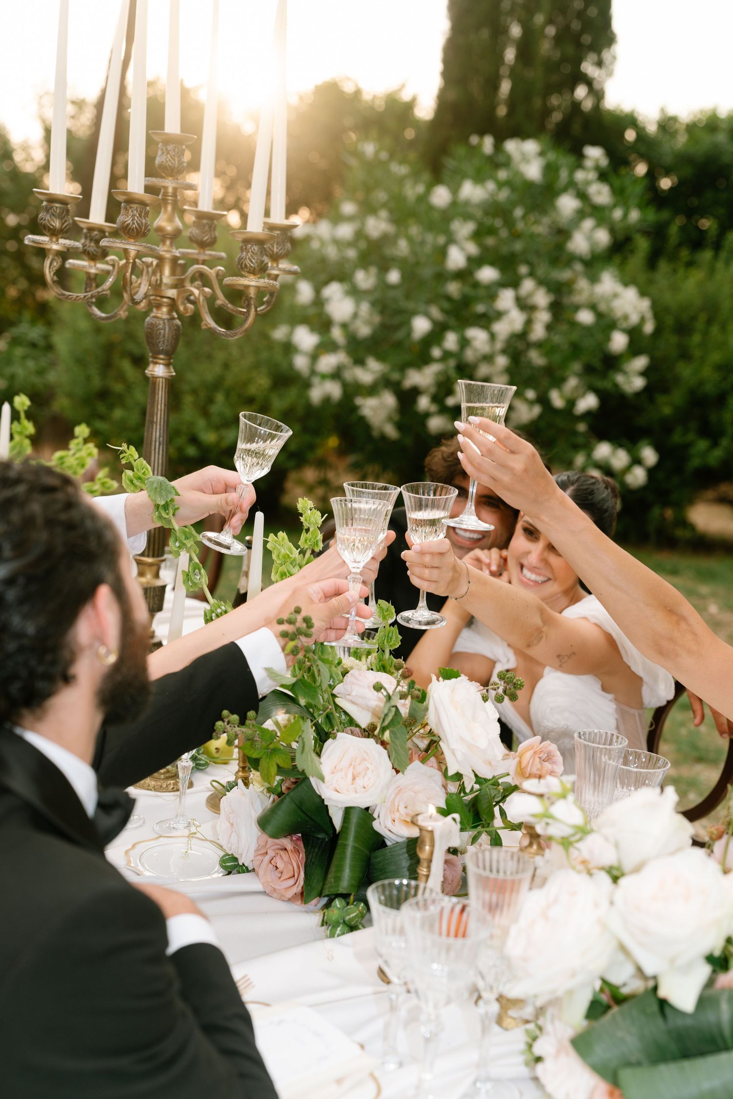 Celebratory toast moment at an outdoor wedding reception with crystal glasses and floral centerpieces.