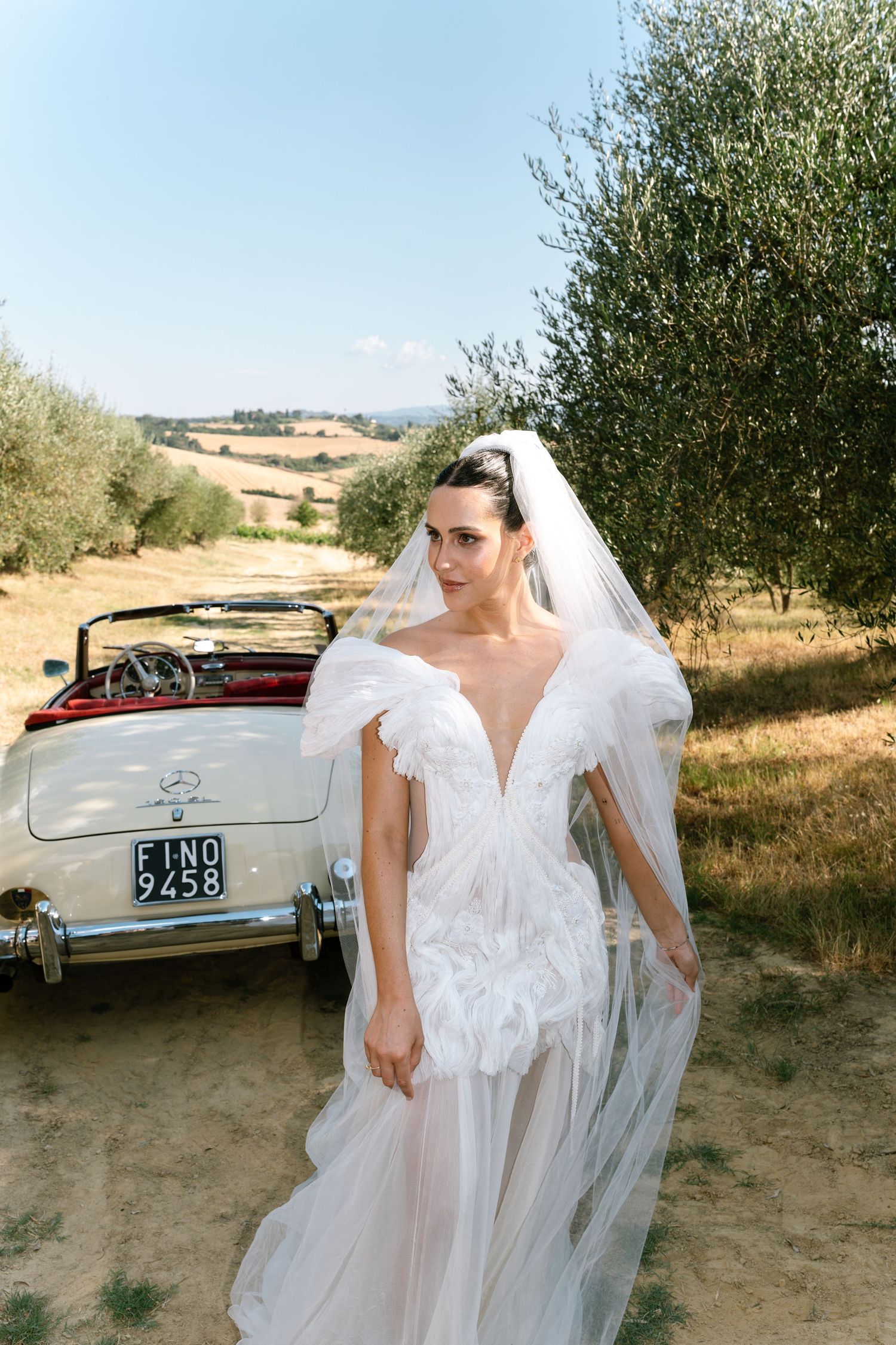An elegant white wedding gown with ruffled details photographed against an olive grove landscape.