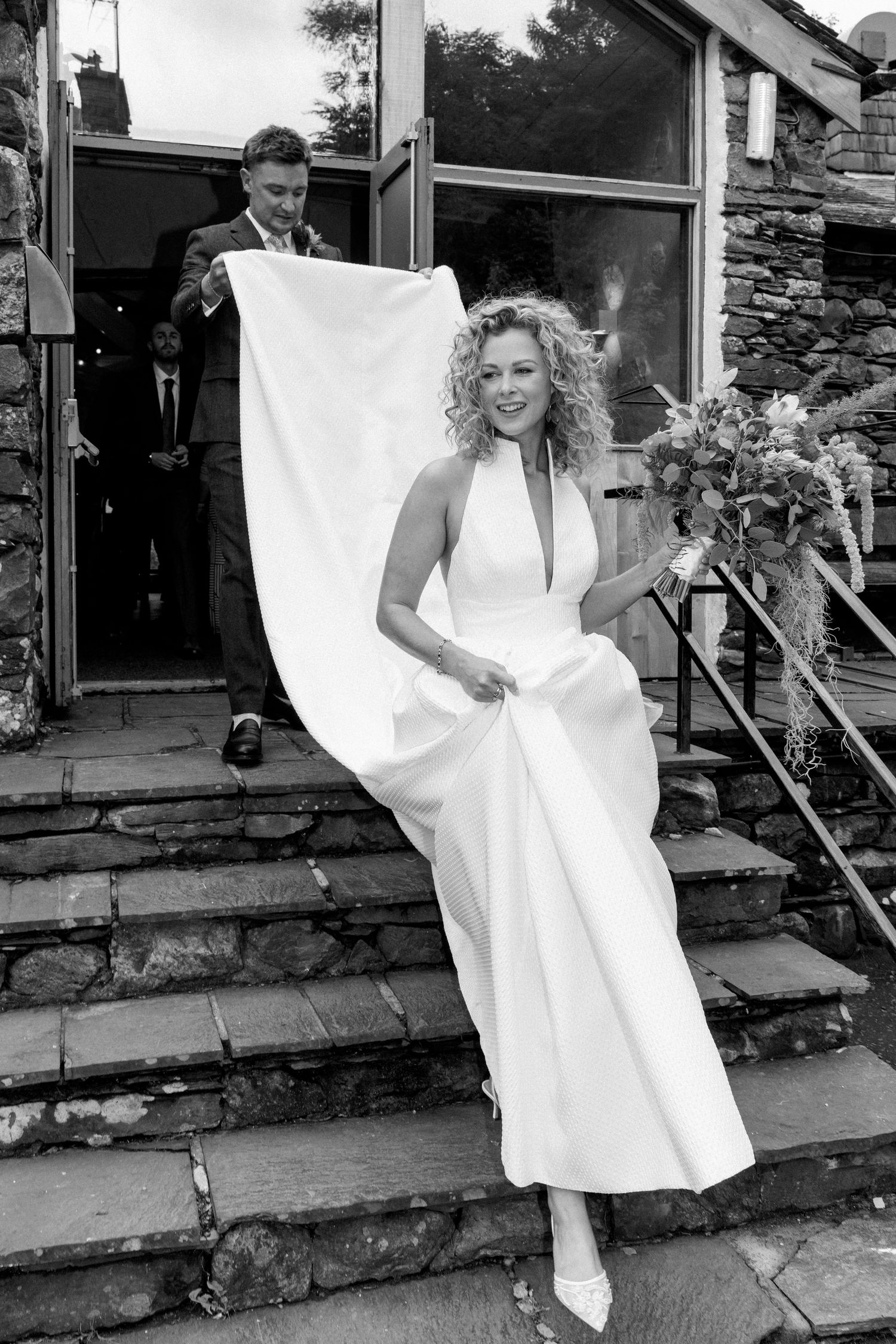 A wedding party dances and celebrates on stone steps with white fabric flowing in the breeze.