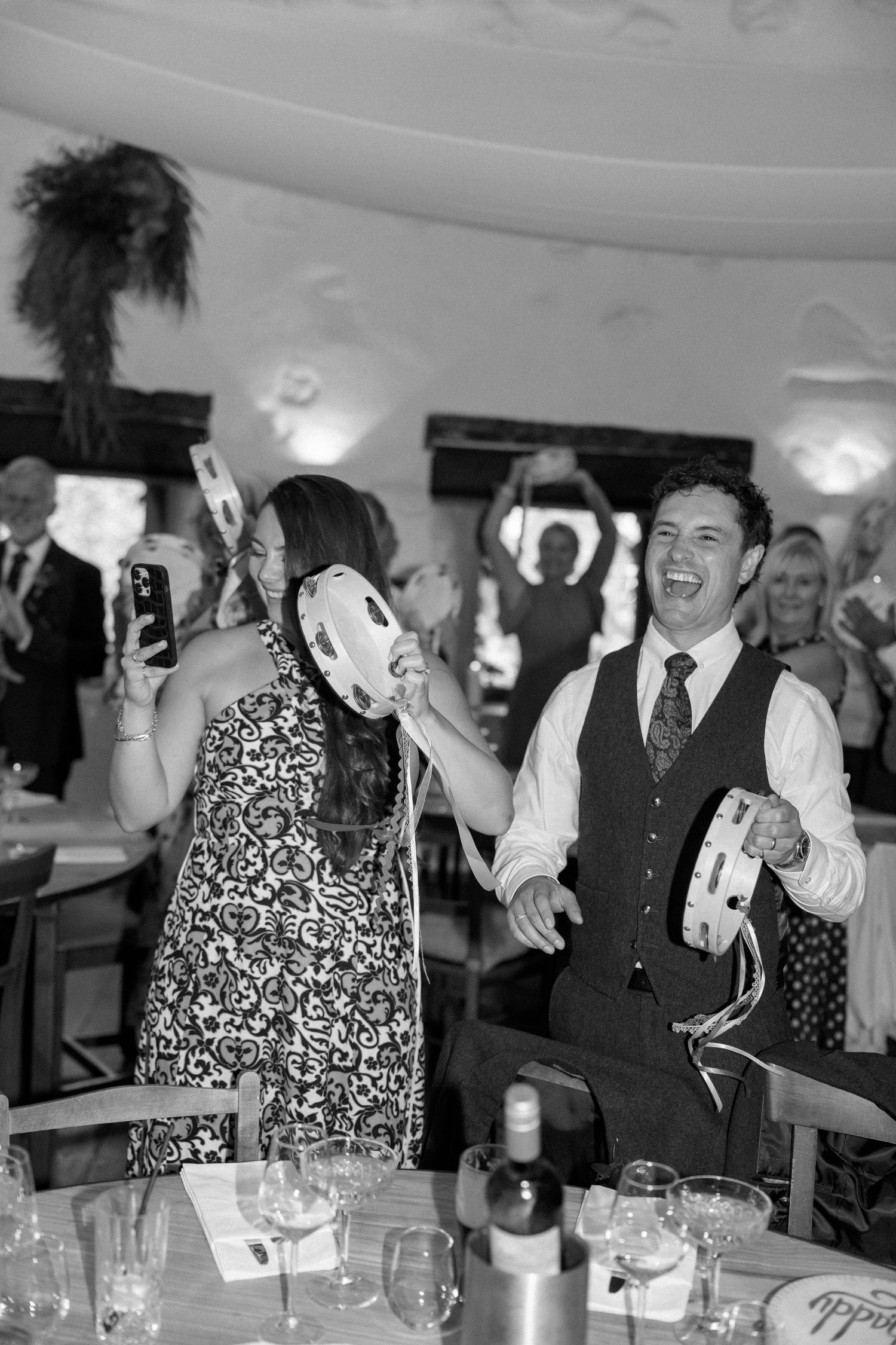 Black and white photo of wedding reception guests laughing and dancing indoors.