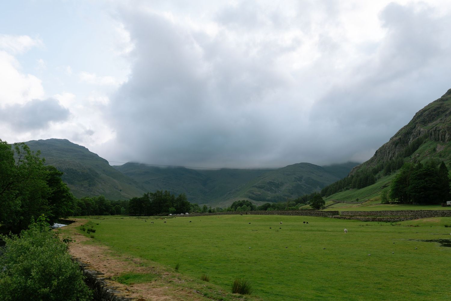 Dramatic cloudy sky over green valley and mountains in rural countryside.