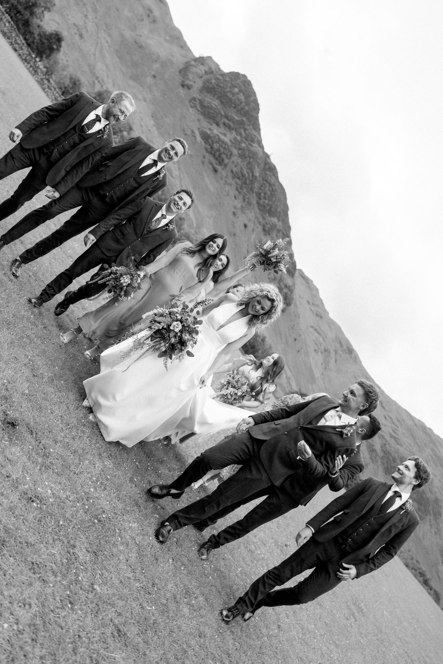 A creative angled black and white photo of a wedding party lined up against a mountain landscape.