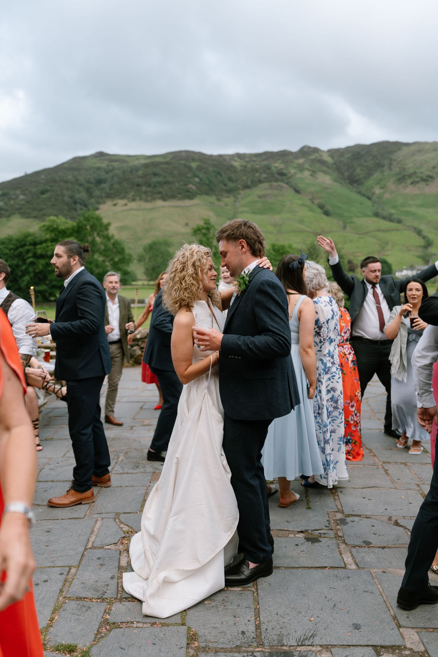 Wedding guests dancing on an outdoor stone patio with mountains visible in the background.