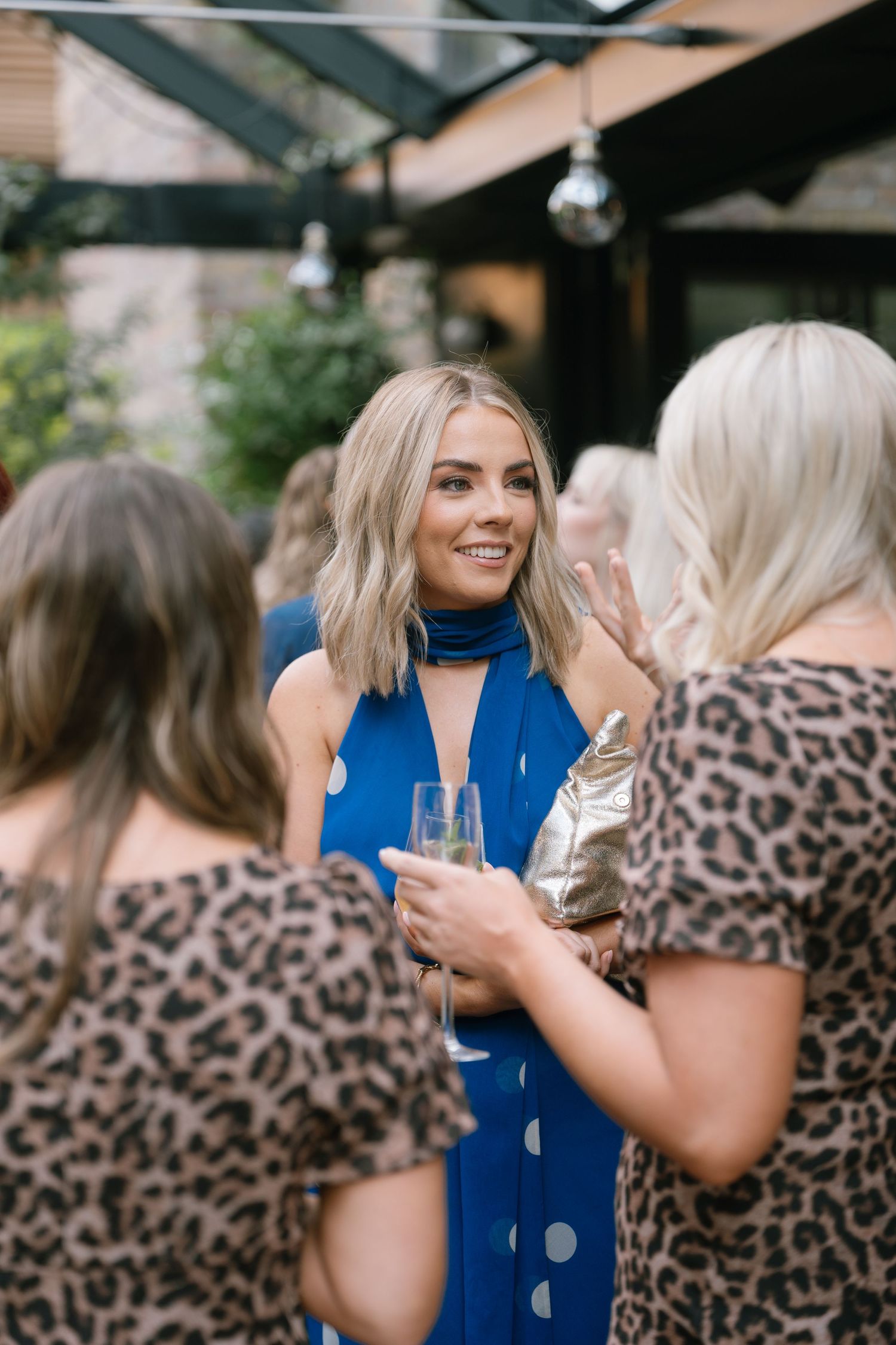 Wedding guests in leopard print and blue outfits chatting and laughing together.