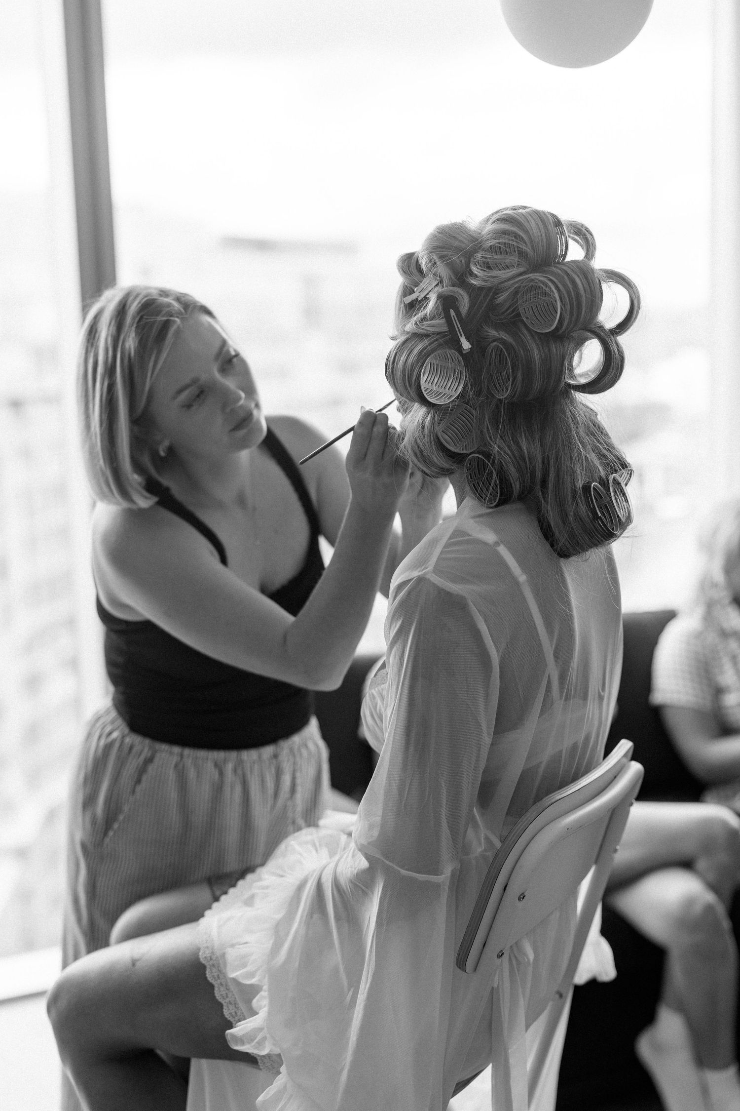 Black and white photo of wedding preparation with hair styling in progress.