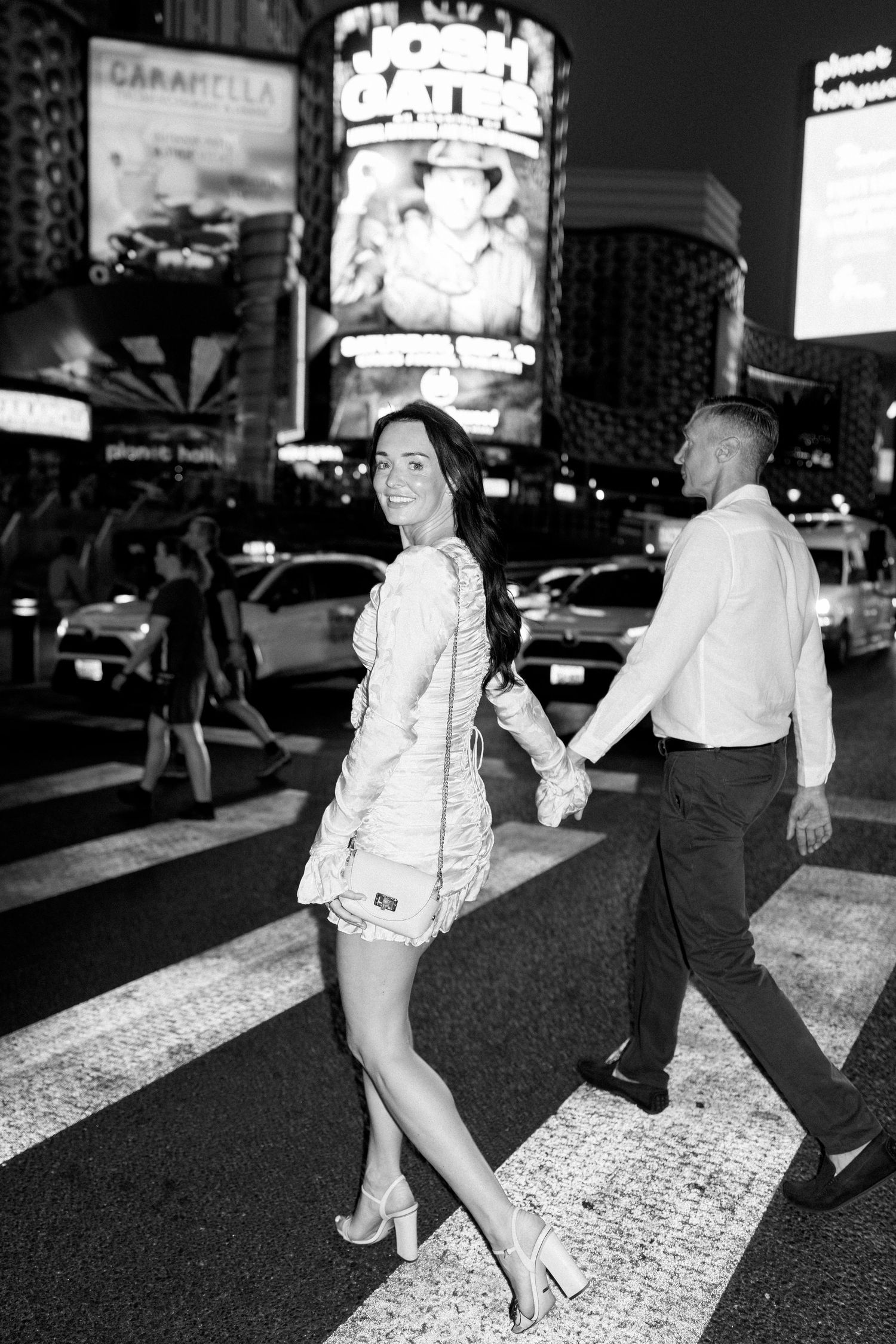 A black and white photo of a couple crossing a street in Las Vegas at night.